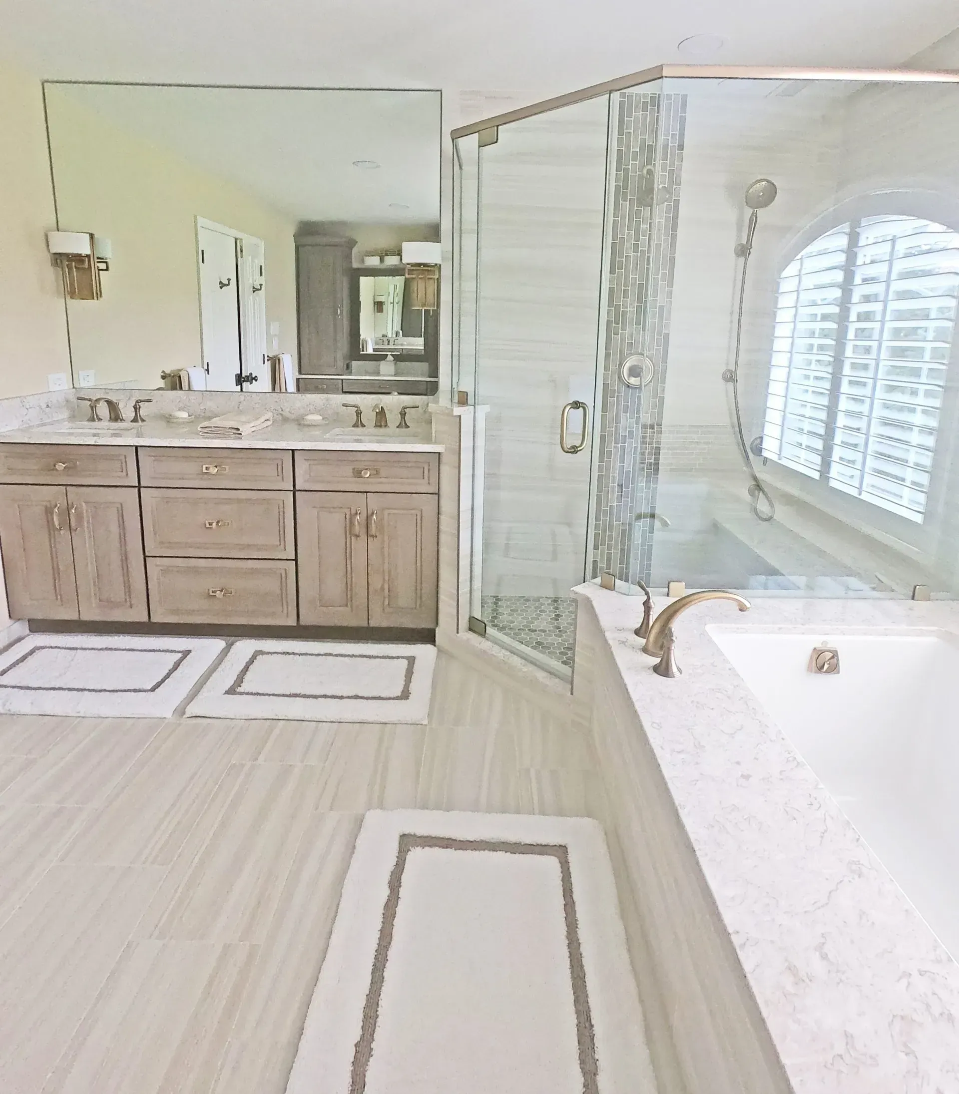 Bright bathroom with double vanity, large mirror, glass shower, and freestanding tub with window shutters  In Bucks County PA