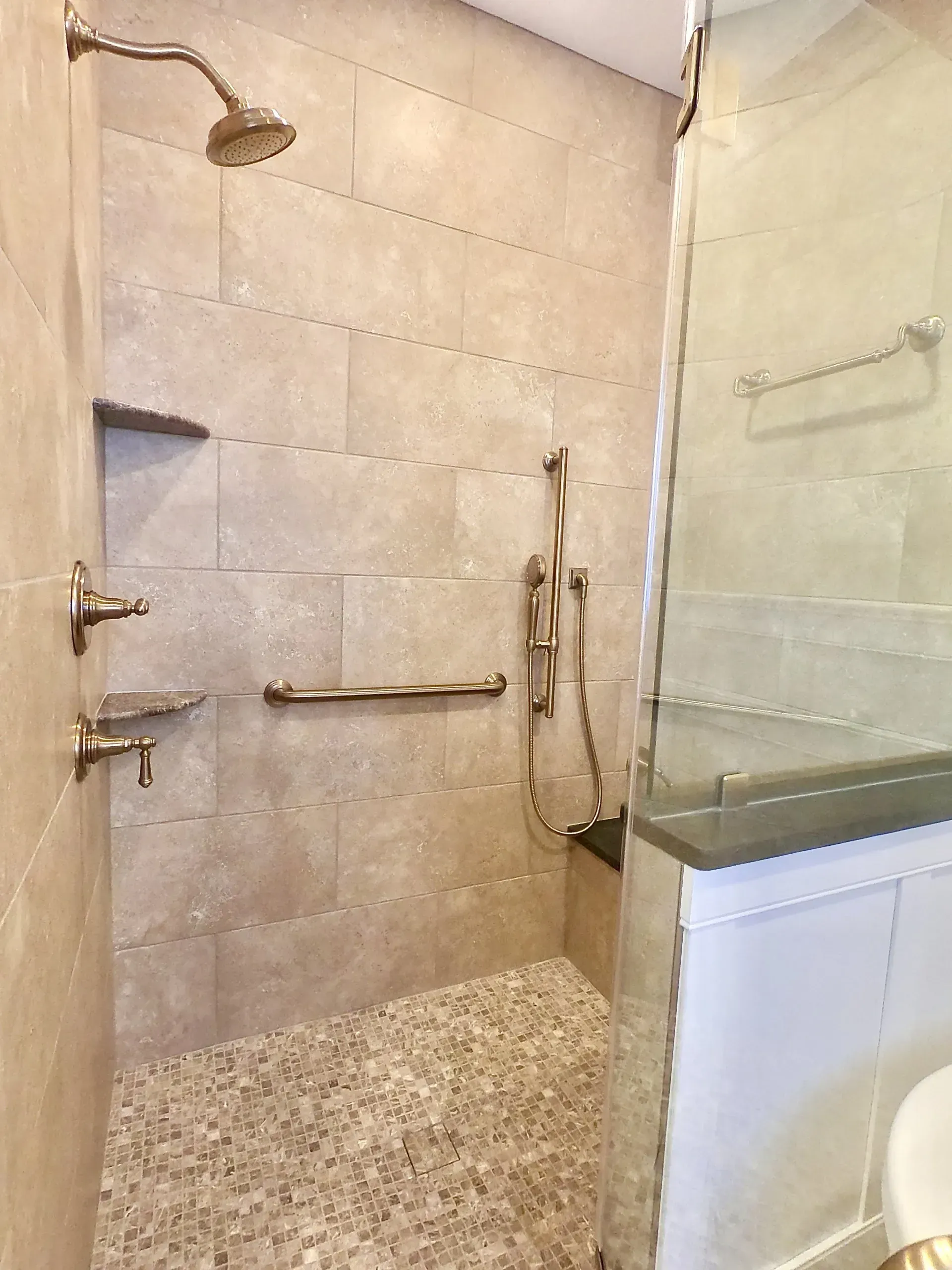 Spacious tiled walk-in shower with pebble floor, glass divider, grab bars, and wall-mounted showerhead  In Bucks County PA