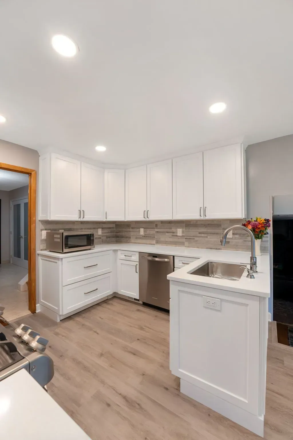 Bright modern kitchen with white cabinets, wood floor, and a small island with sink and flowers In Bucks Country PA