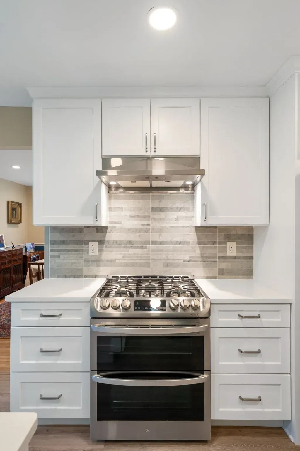 Modern white kitchen with gas range, stainless hood, and gray tile backsplashin Bucks County PA