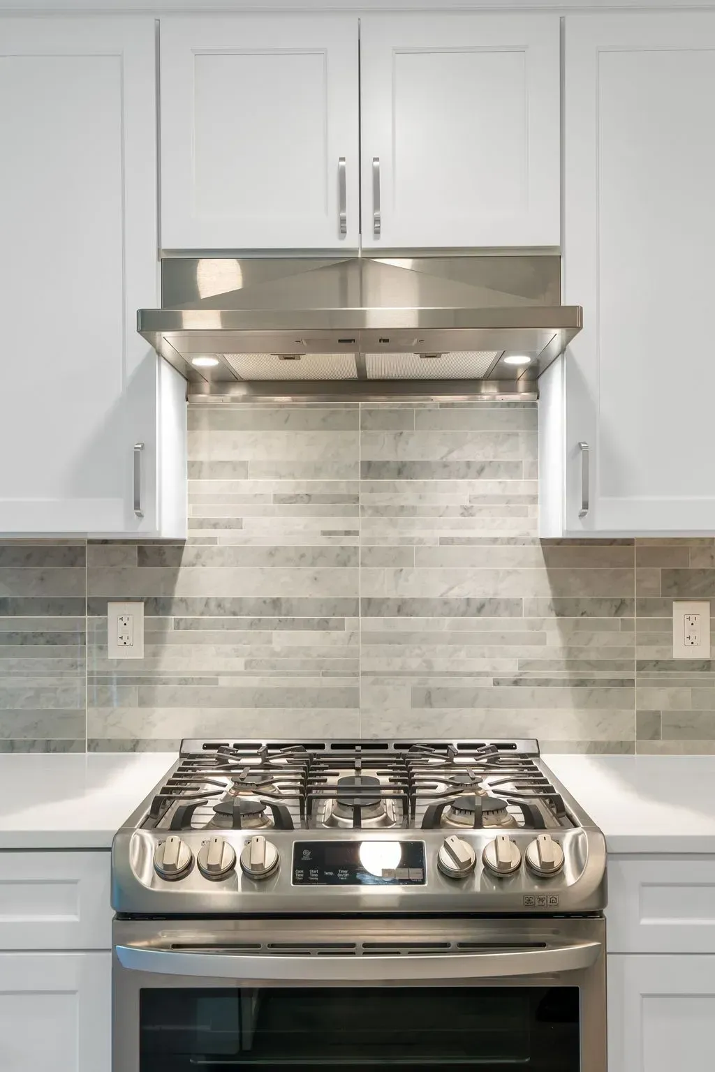 Modern kitchen with stainless steel gas range and hood beneath white cabinets and tiled backsplashin Bucks County PA