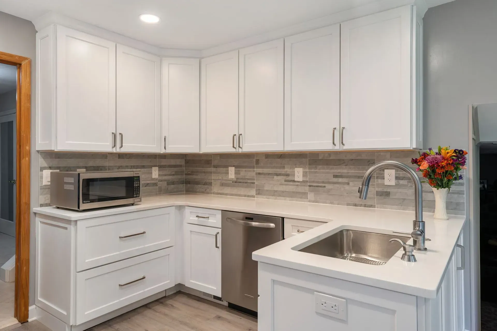 Bright white kitchen with white cabinets, gray backsplash, stainless sink, and flowers on the counter in Bucks County PA
