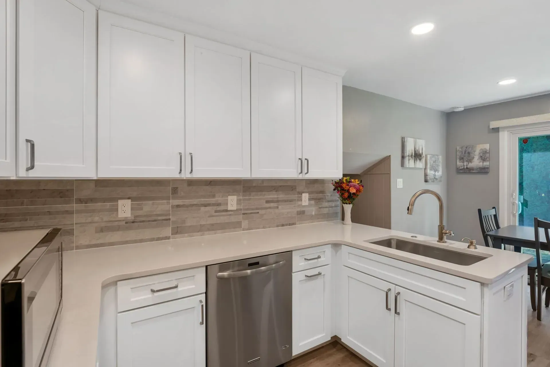 Modern white kitchen with tiled backsplash, stainless appliances, and a sink by a bright window in Bucks County PA