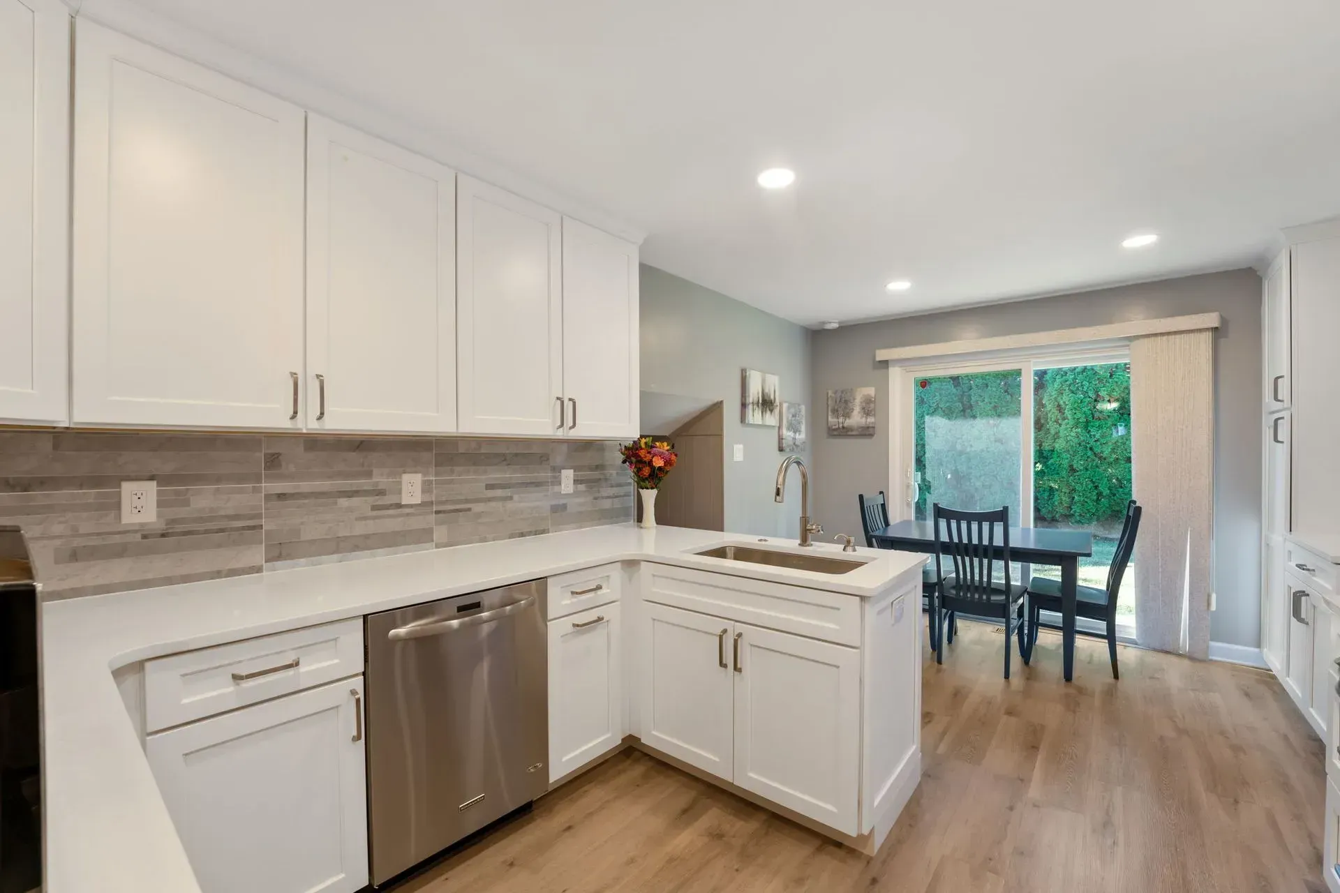 Bright white kitchen with stainless appliances, island, and dining area by glass doors opening to greenery in Bucks County PA