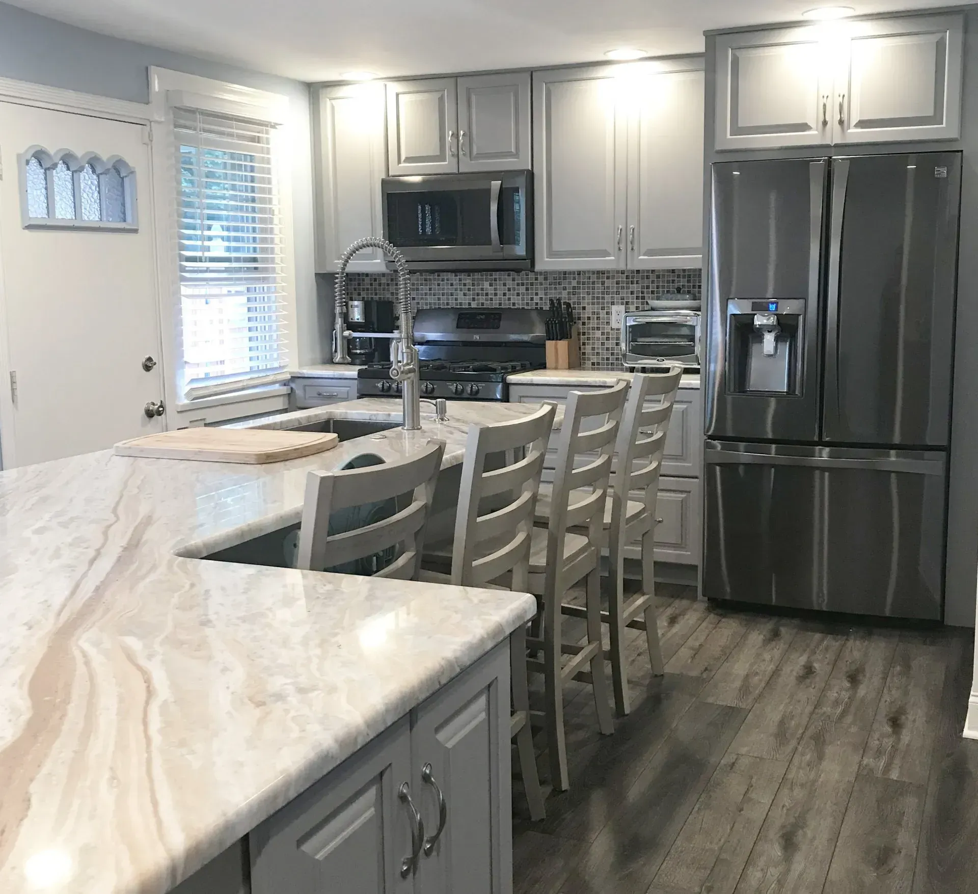 Modern gray-and-white kitchen with island, barstools, stainless appliances, and a dining table by the window  In Bucks County PA