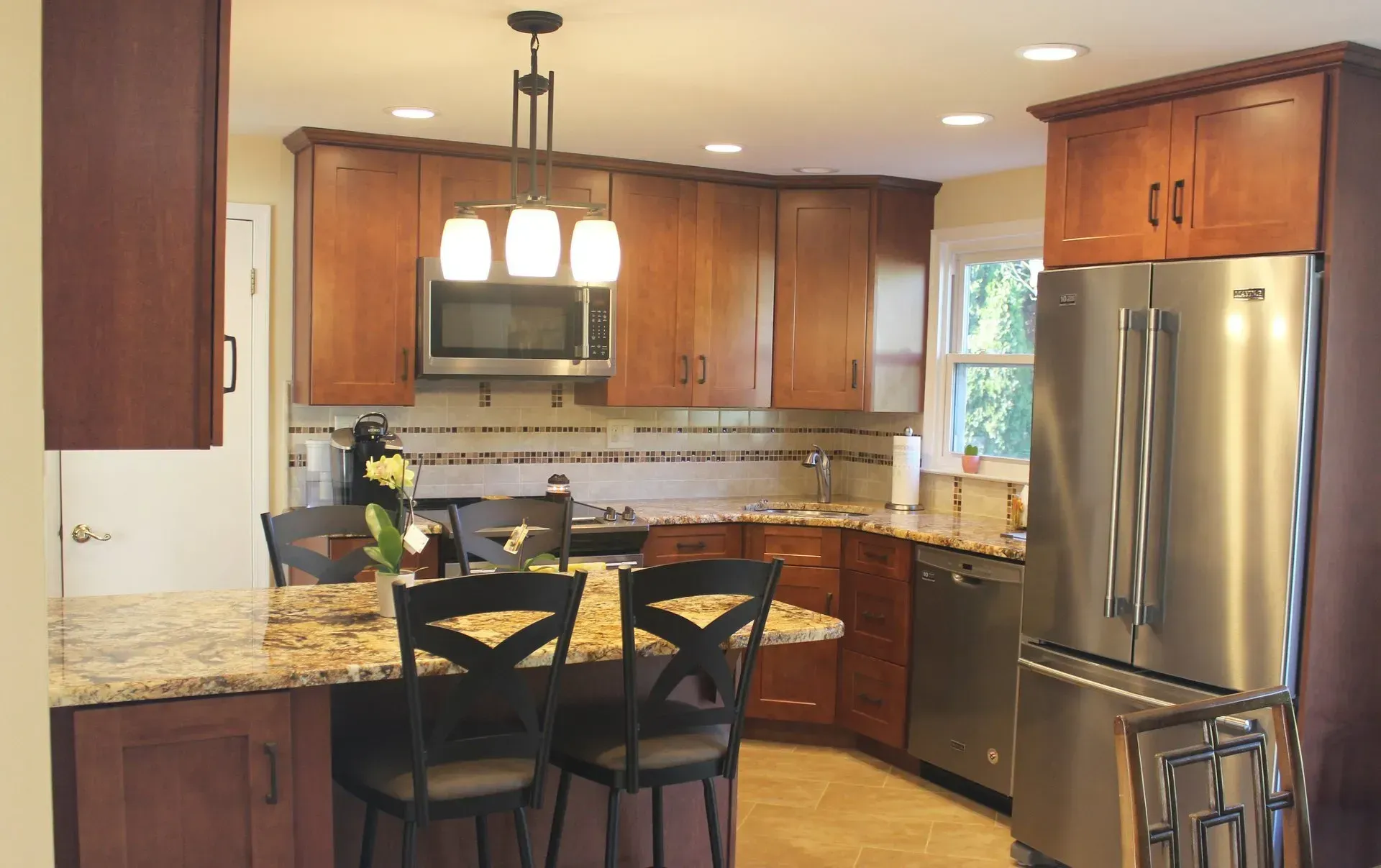 Warm kitchen with wood cabinets, granite island, stainless steel fridge, and two black bar stools In Bucks Country PA