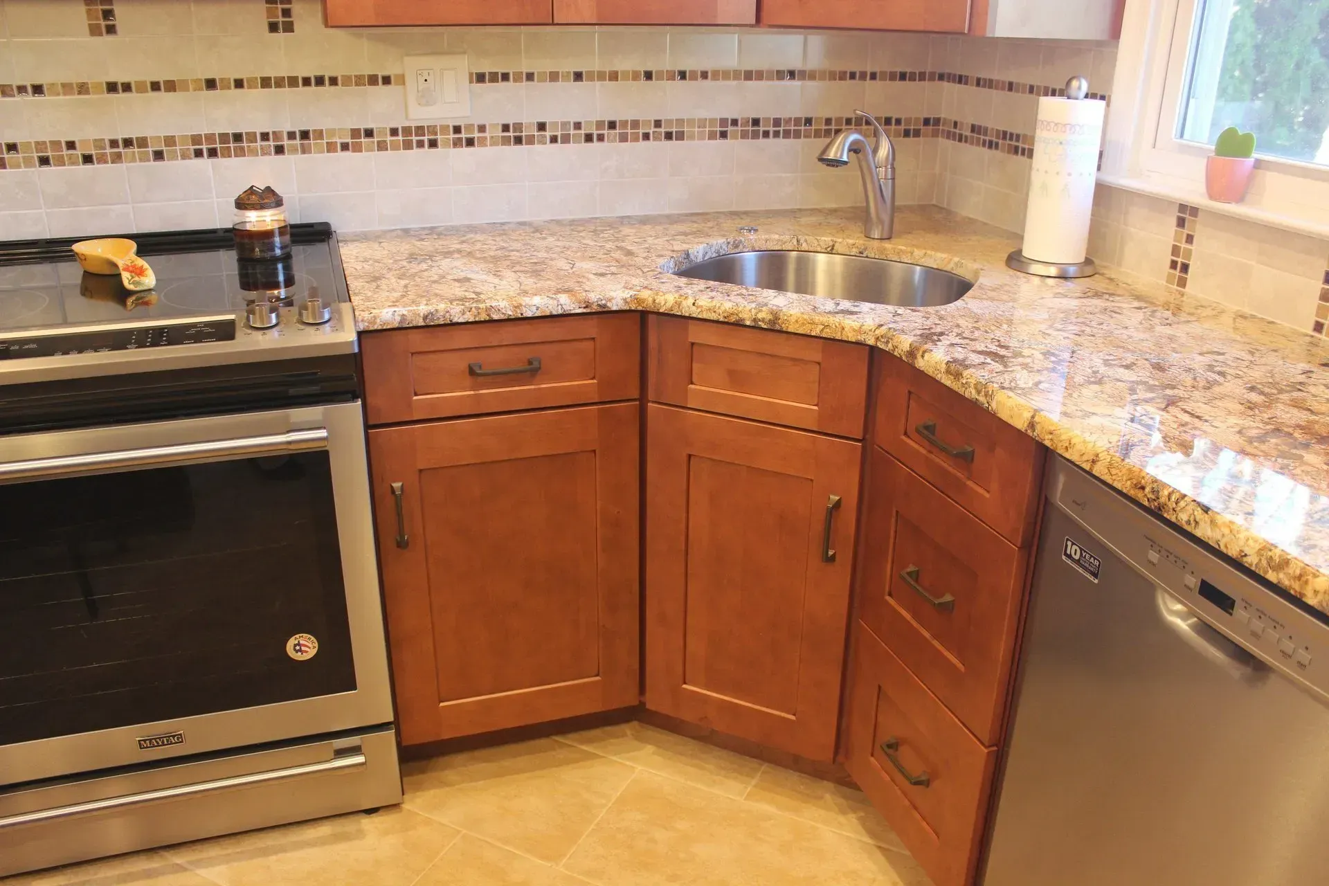 Modern kitchen corner with granite countertop, wooden cabinets, sink, stove, and dishwasher In Bucks County PA