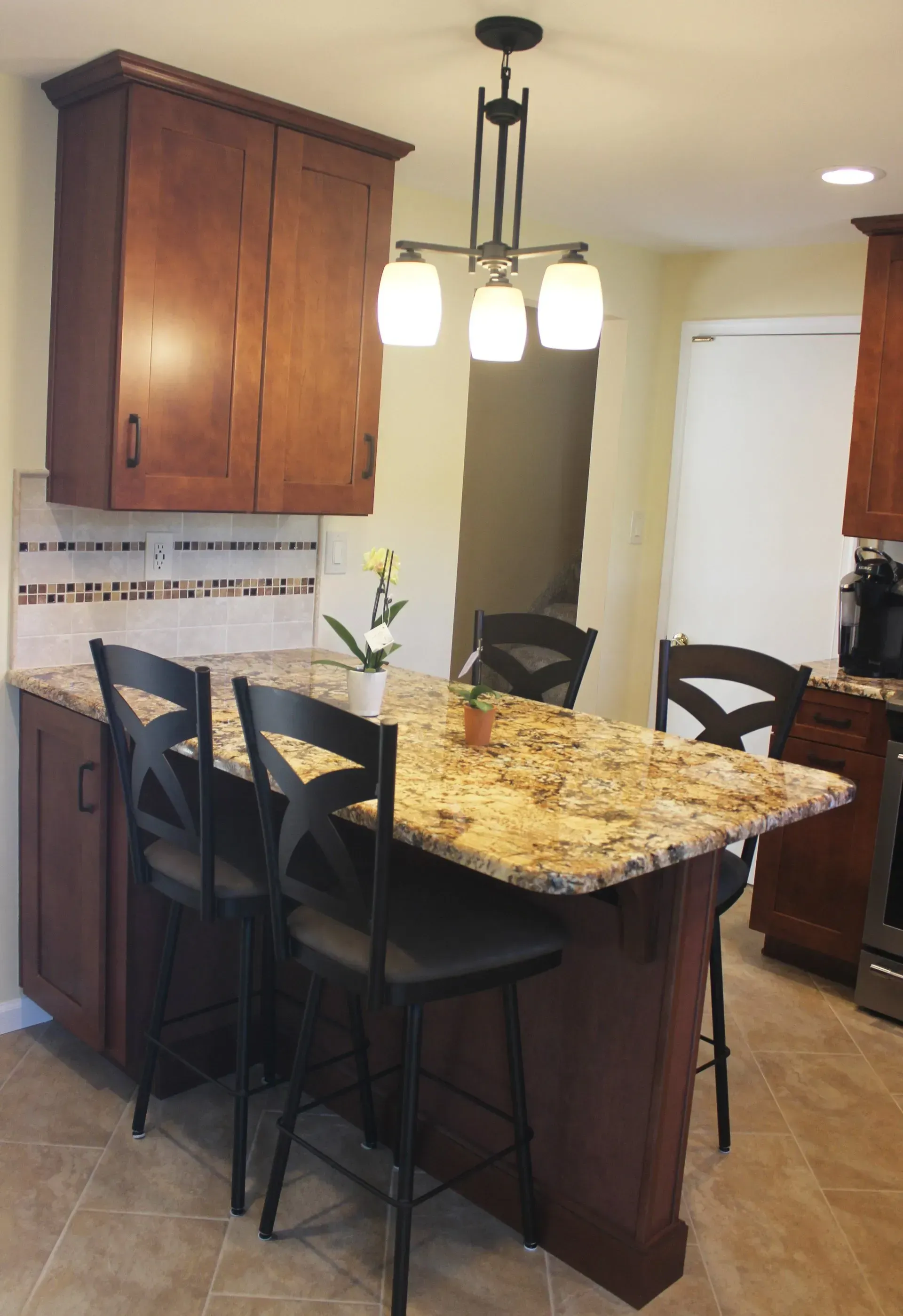 Kitchen with granite island, four black bar stools, wood cabinets, and hanging pendant lights In Bucks County PA