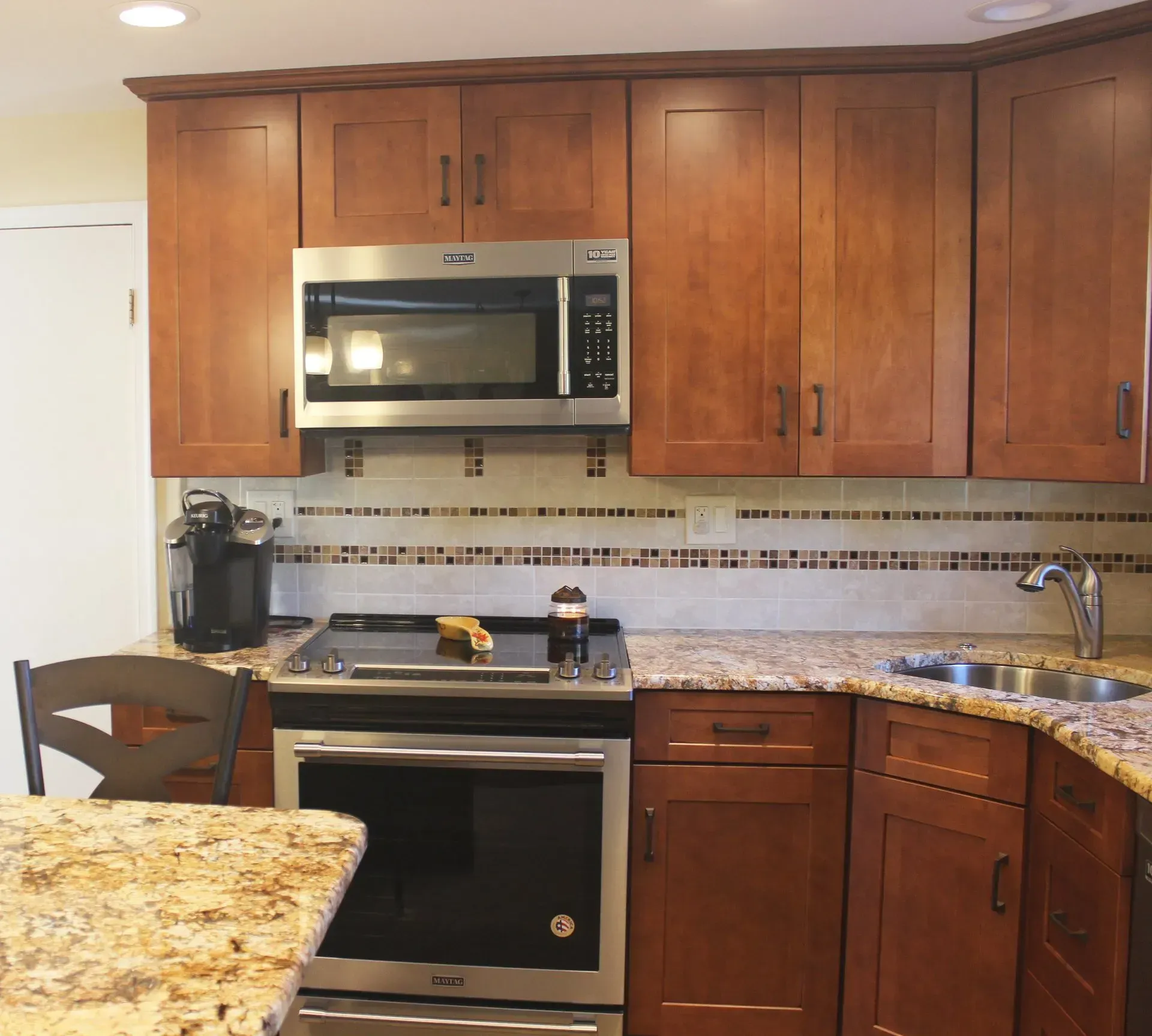 Modern kitchen with wooden cabinets, granite countertops, stainless steel microwave, stove, and coffee maker In Bucks County PA