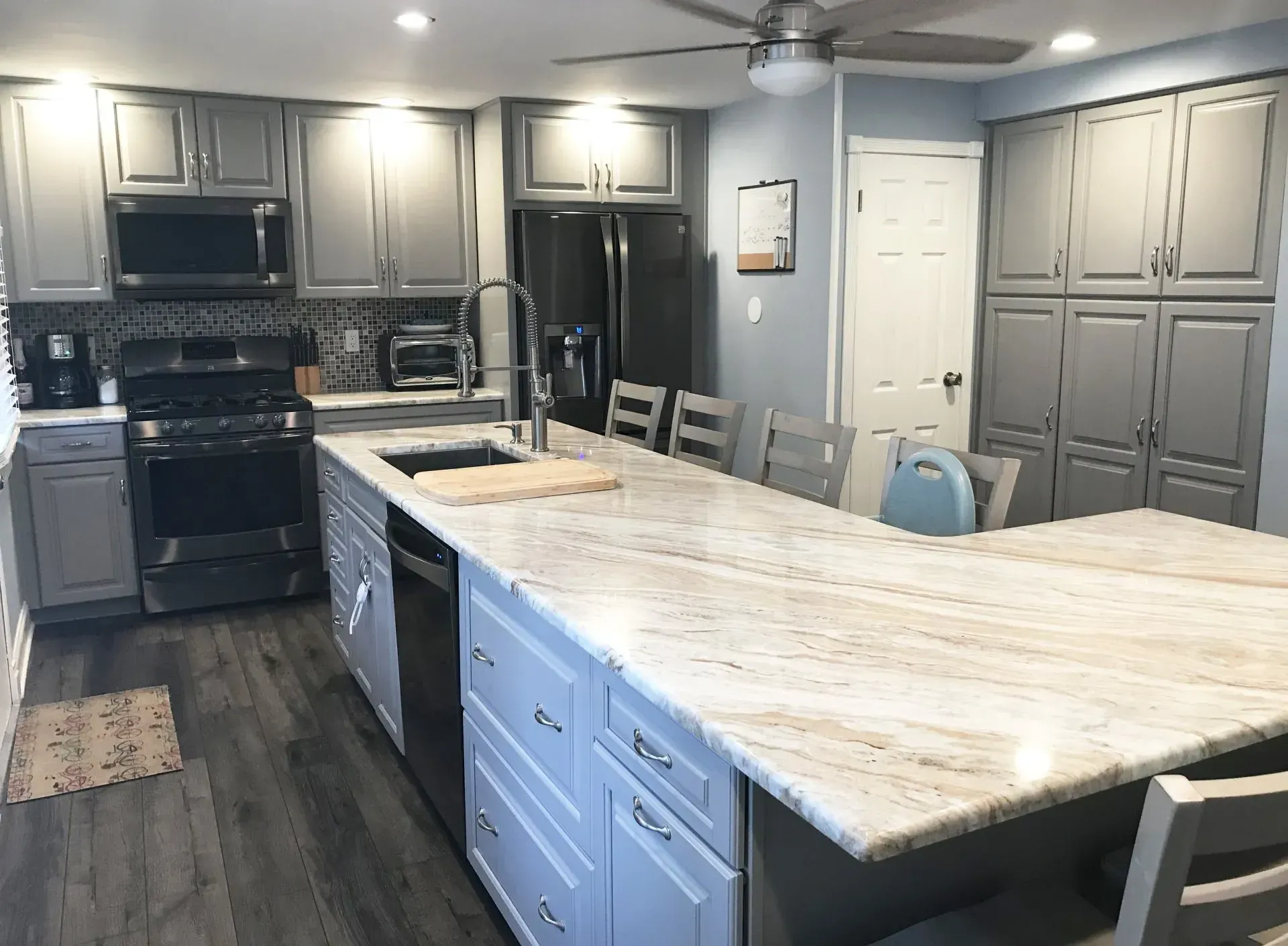 Modern kitchen with gray cabinets, black appliances, and a large white island with chairs In Bucks Country PA