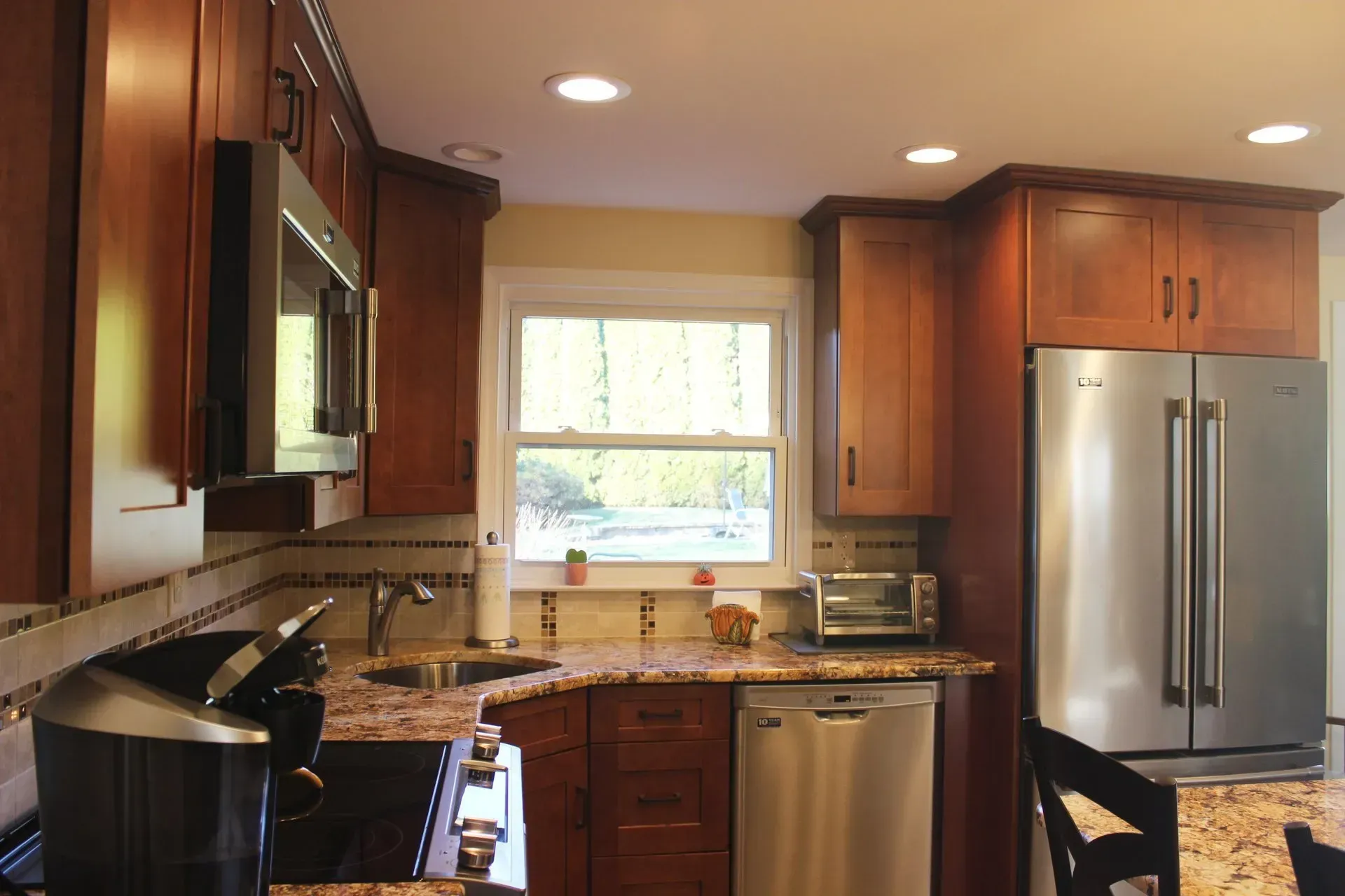Modern kitchen with wooden cabinets, stainless steel fridge, granite countertops, and a window above the sink In Bucks County PA