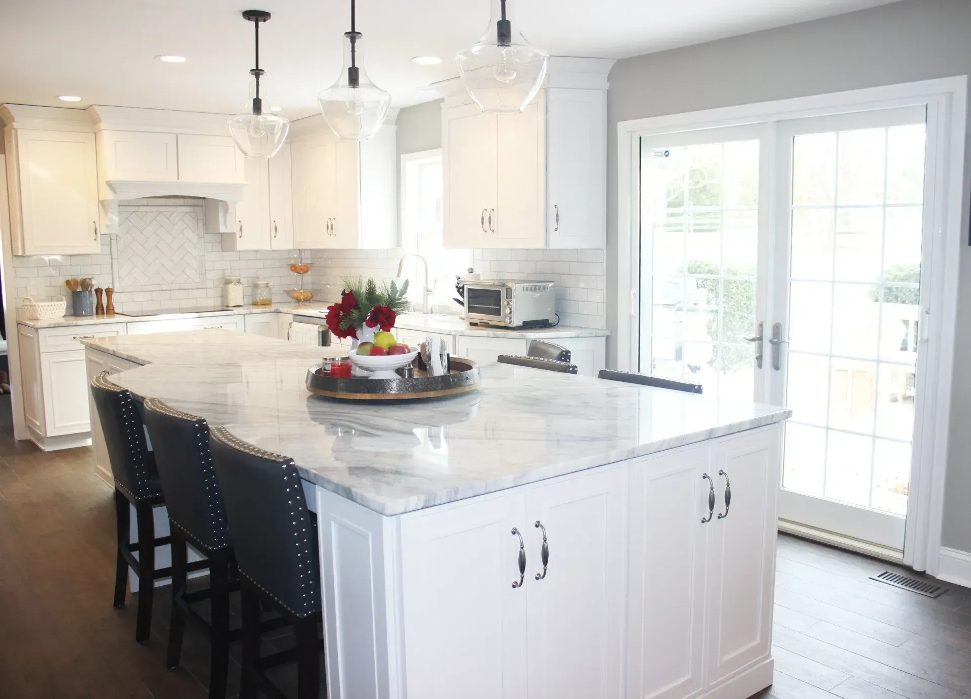 Bright white kitchen with marble island, black stools, pendant lights, and French doors to a patio  In Bucks County PA