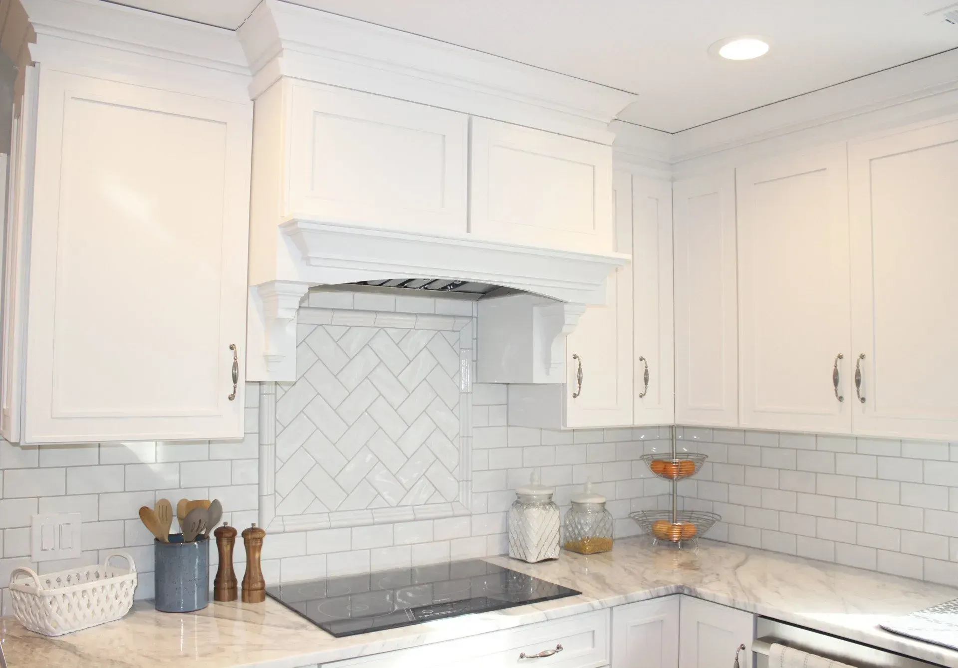 White kitchen with marble countertop, herringbone tile backsplash, and a stainless steel stove under a range hood  In Bucks County PA