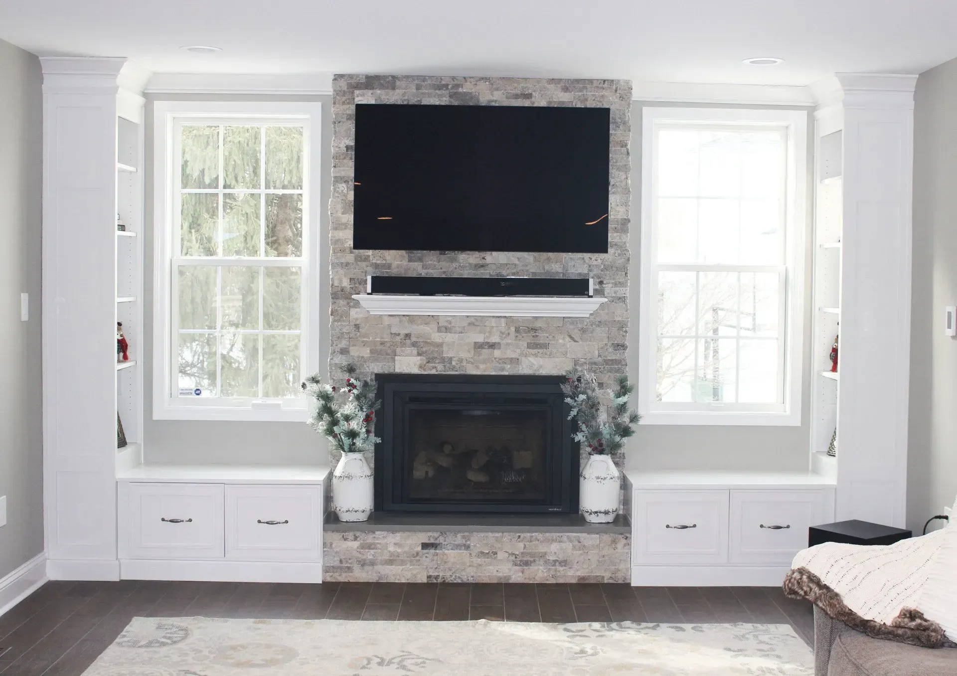 Bright living room fireplace with stone surround, mounted TV, white cabinets, and tall windows  In Bucks County PA