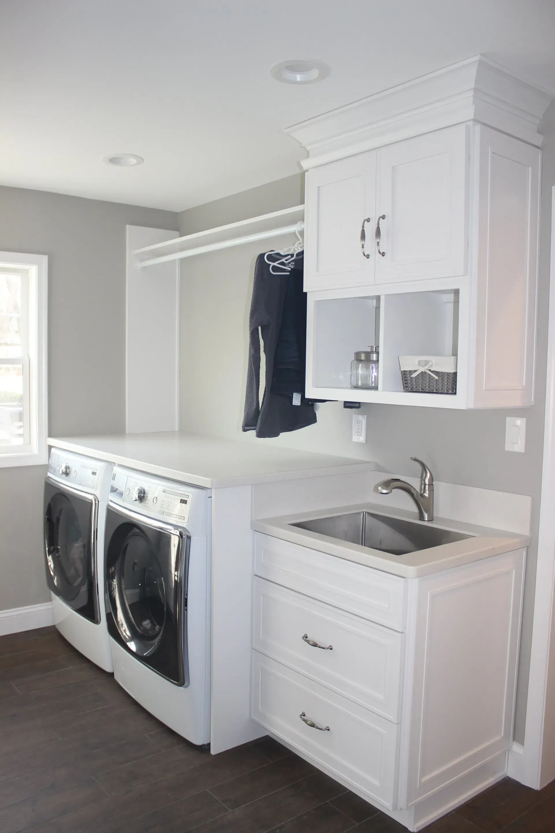 Laundry room with stacked washer and dryer, white cabinets, sink, and hanging clothes line In Bucks County PA