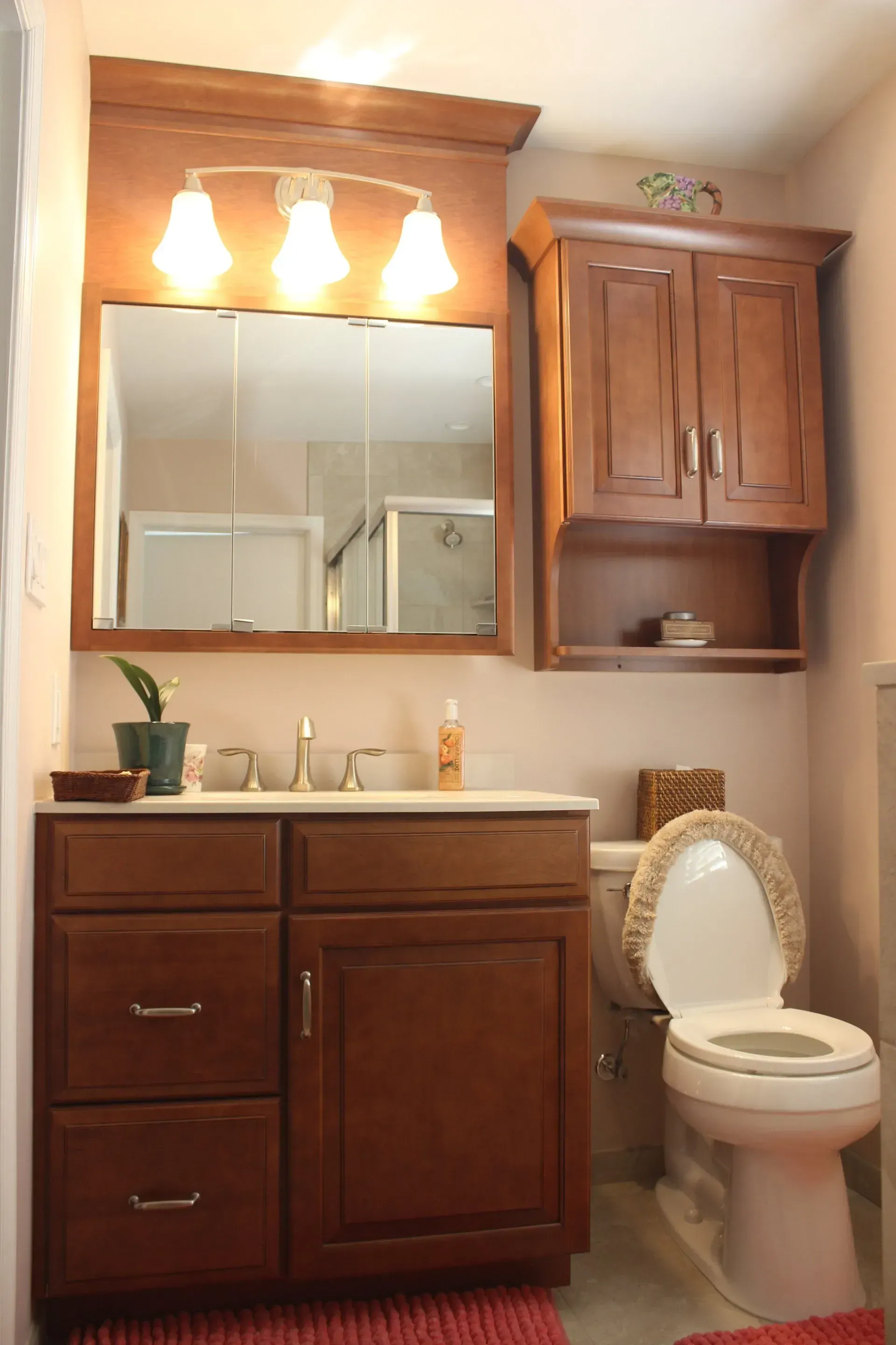 Small bathroom with wood vanity, mirror lights, cabinet, and toilet beside the sink In Bucks County PA