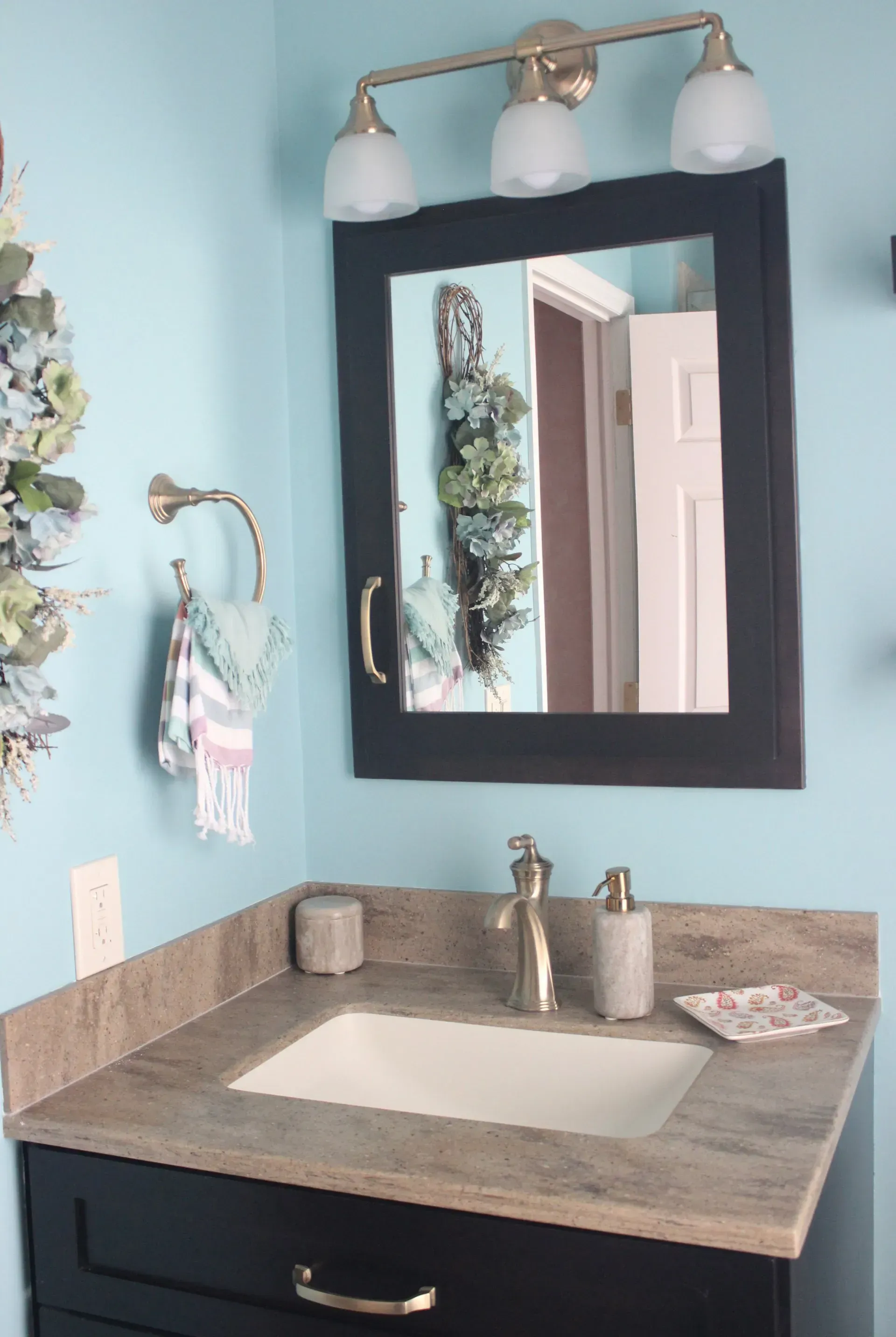 Small bathroom vanity with dark cabinet, stone countertop, mirror, and two-light fixture against a light blue wall In Bucks County PA