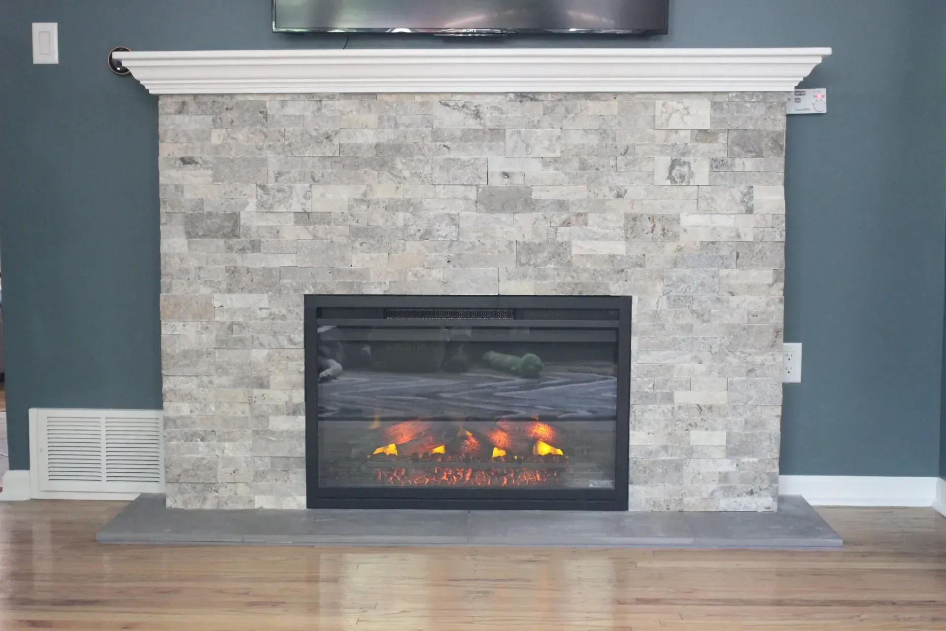 Stone fireplace with electric flames in a modern living room, framed by a white mantel and dark gray wall  In Bucks County PA