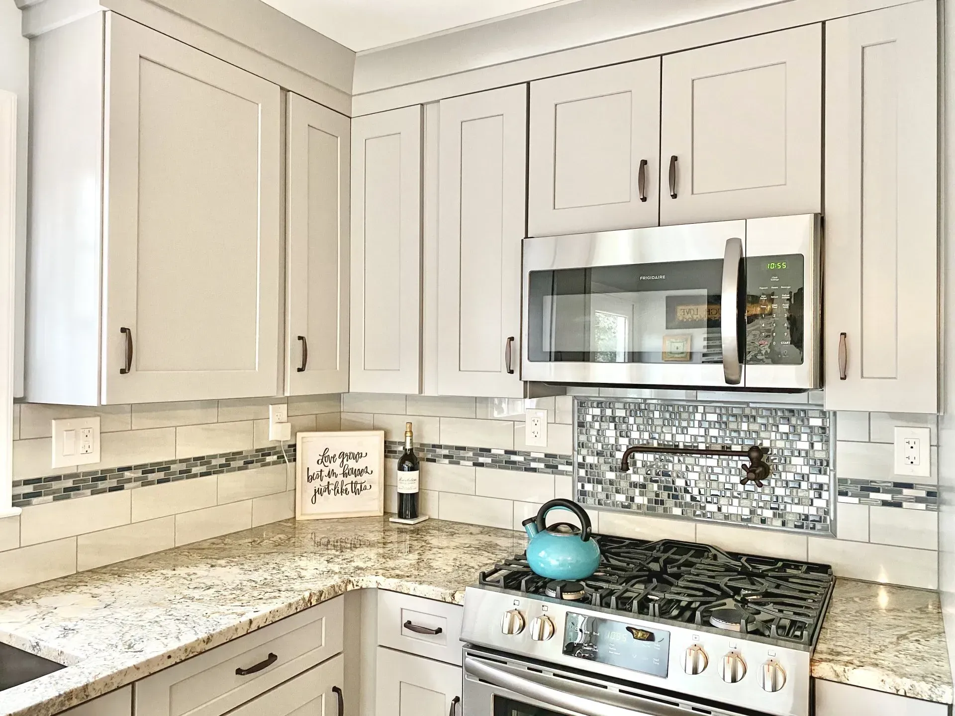 Bright white kitchen with granite countertops, mosaic backsplash, stainless appliances, and a blue kettle on the stove  In Bucks County PA