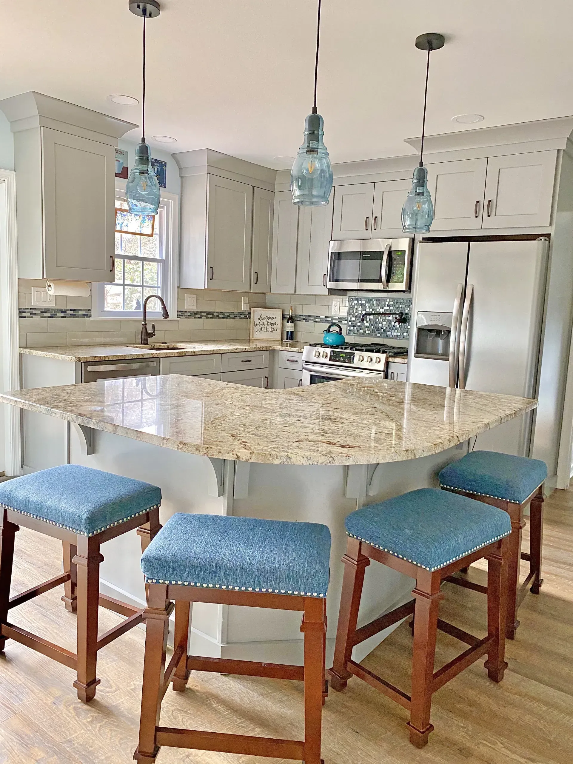 Bright kitchen with a large granite island, blue stools, pendant lights, and stainless steel appliances  In Bucks County PA
