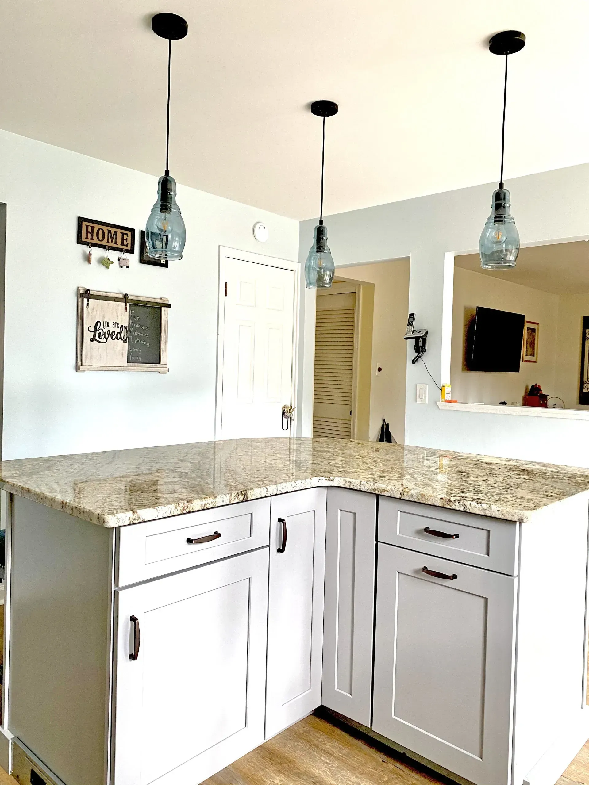 Bright kitchen corner with white and gray cabinets, granite countertops, and three hanging pendant lights  In Bucks County PA