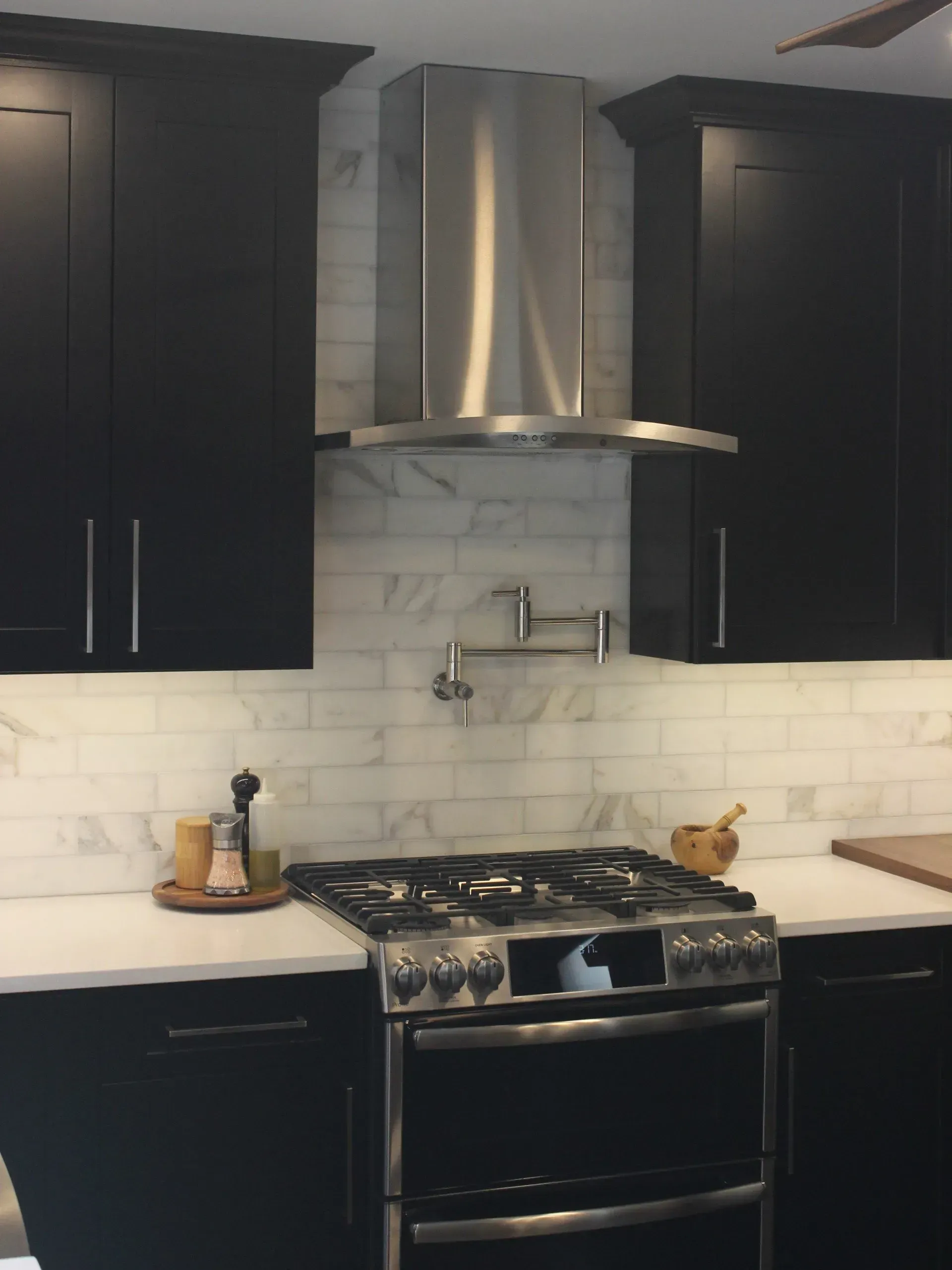 Modern kitchen with black cabinets, white tile backsplash, stainless range hood, and gas stove in Bucks County PA