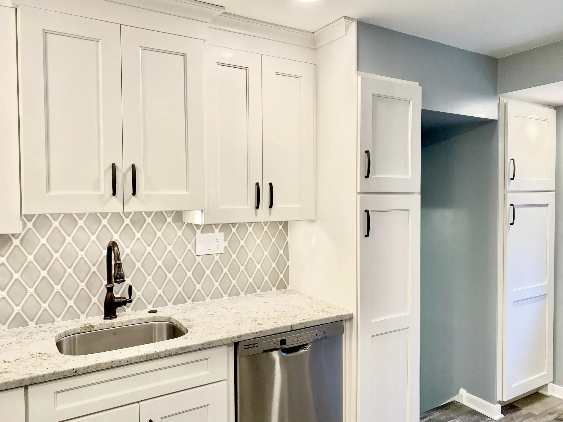 White kitchen with cabinets, patterned backsplash, sink, dishwasher, and open pantry nook In Bucks County PA