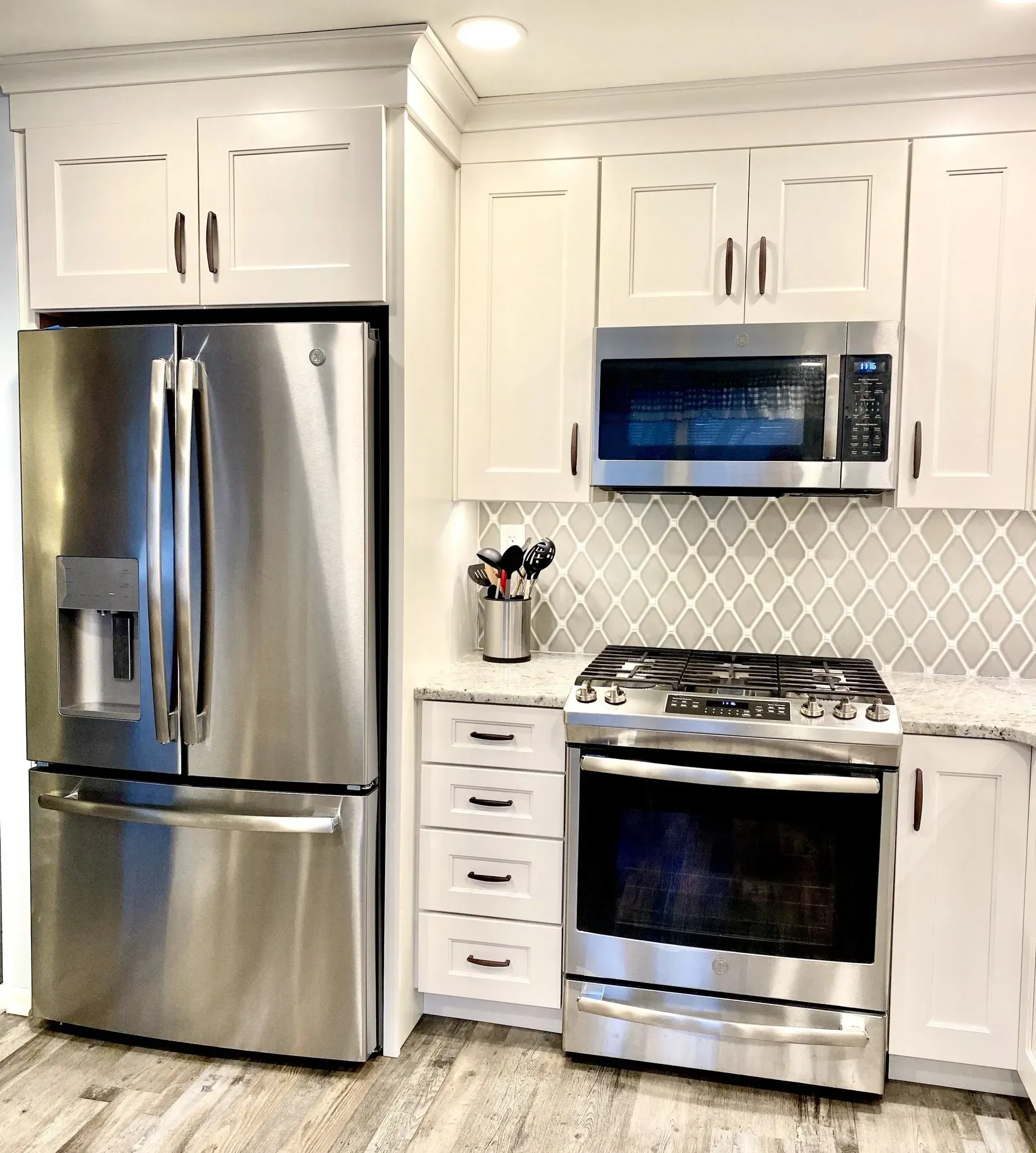 Bright white kitchen with stainless steel fridge, microwave, and stove against a tiled backsplash In Bucks County PA