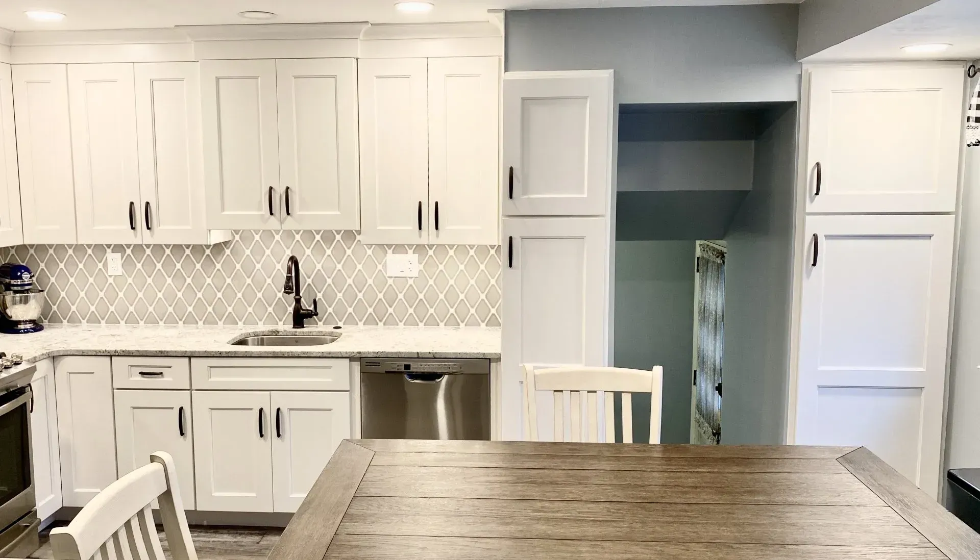 Bright white kitchen with cabinets, tiled backsplash, stainless sink, and wooden table in foreground In Bucks County PA