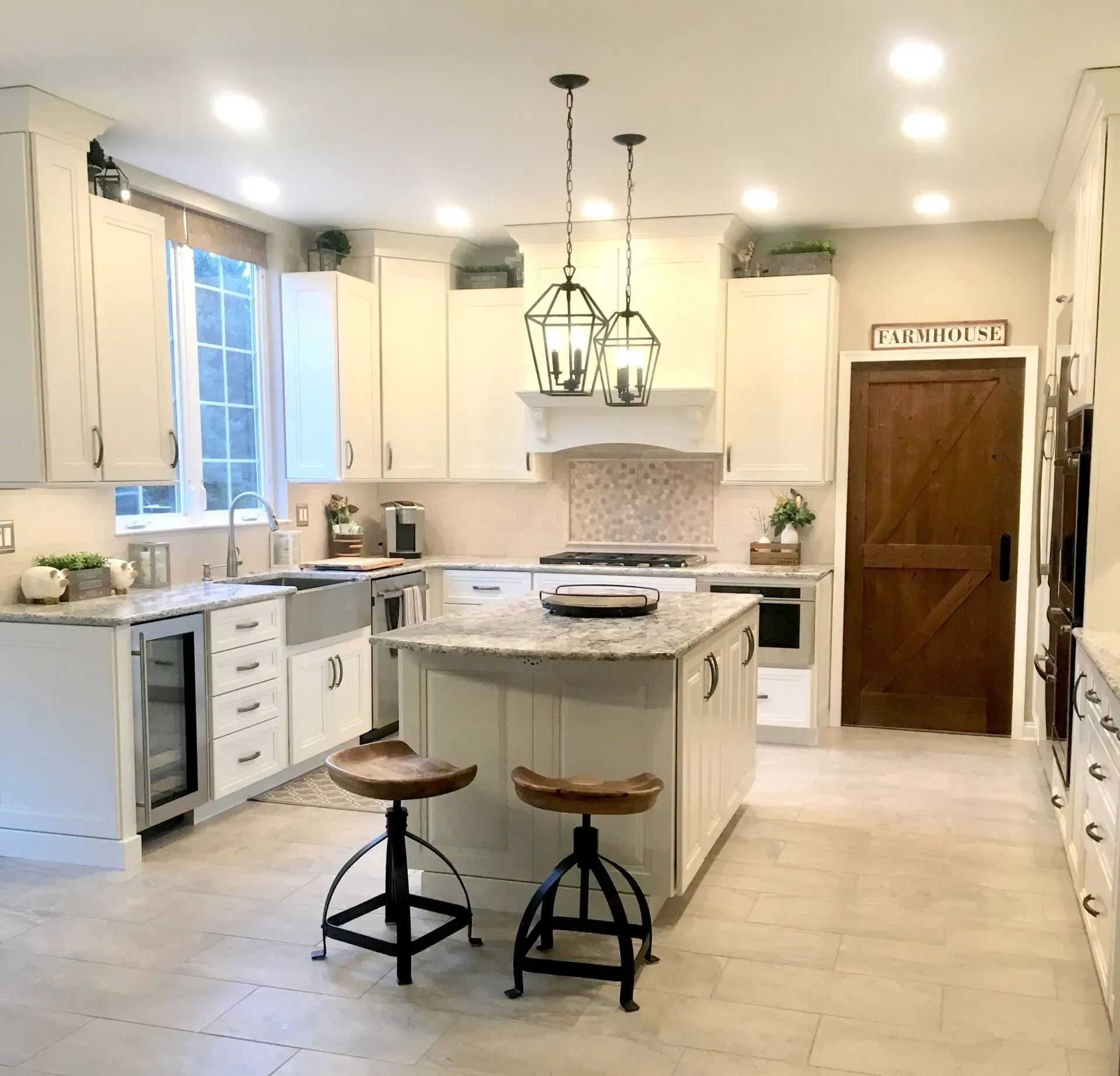 Bright white farmhouse kitchen with island, two stools, pendant lights, and wooden door In Bucks County PA
