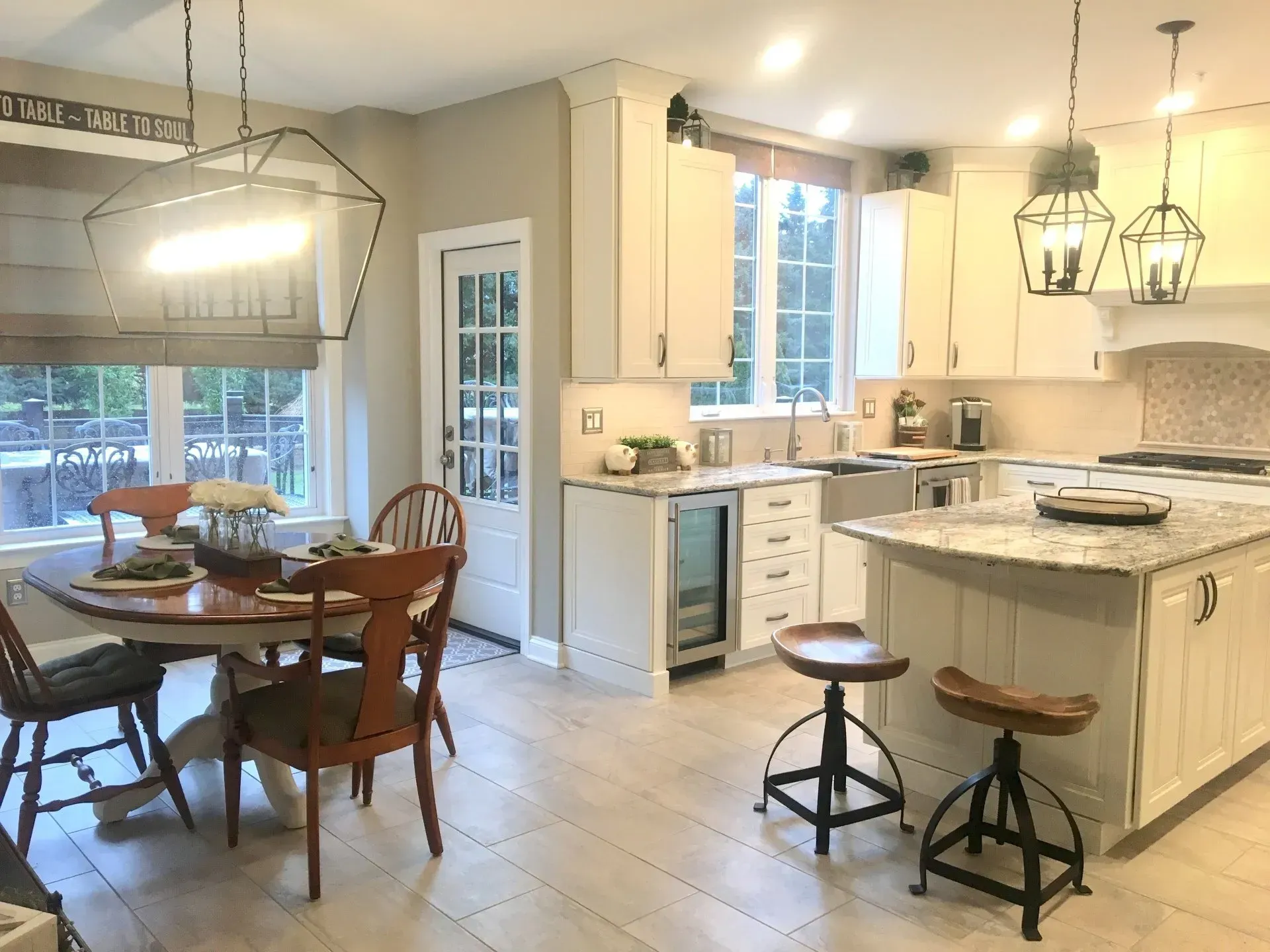Bright kitchen with island, pendant lights, dining table, and stools by a sunlit window and door In Bucks County PA