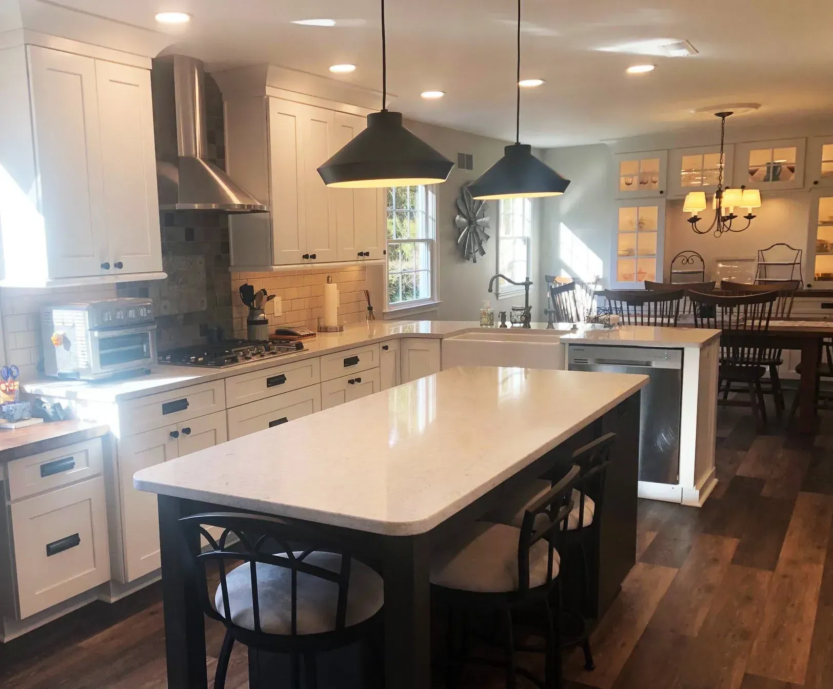 Bright modern kitchen with white cabinets, large island, pendant lights, and dining area in background In Bucks Country PA
