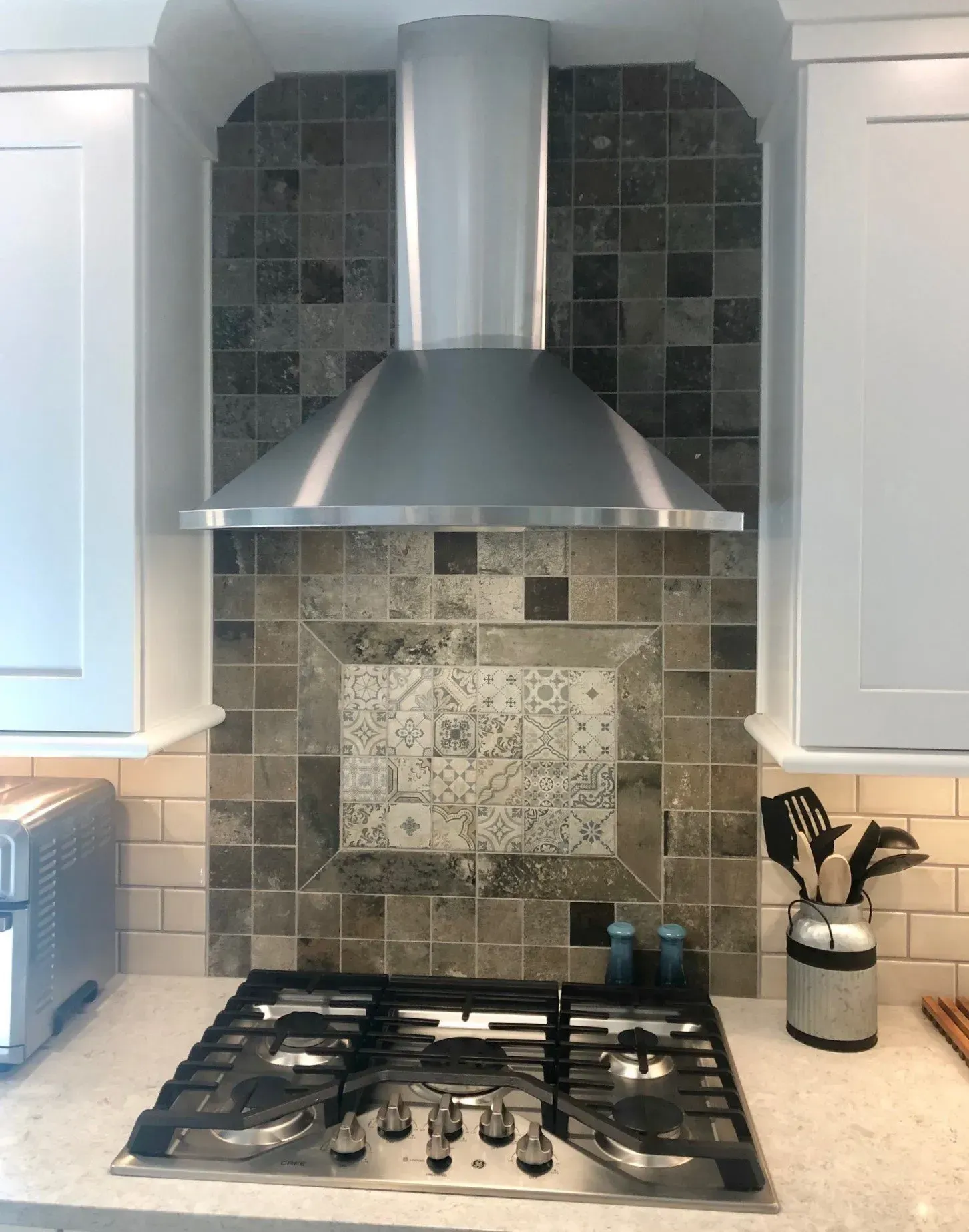 Modern kitchen stove with stainless steel range hood and tiled backsplash In Bucks County PA