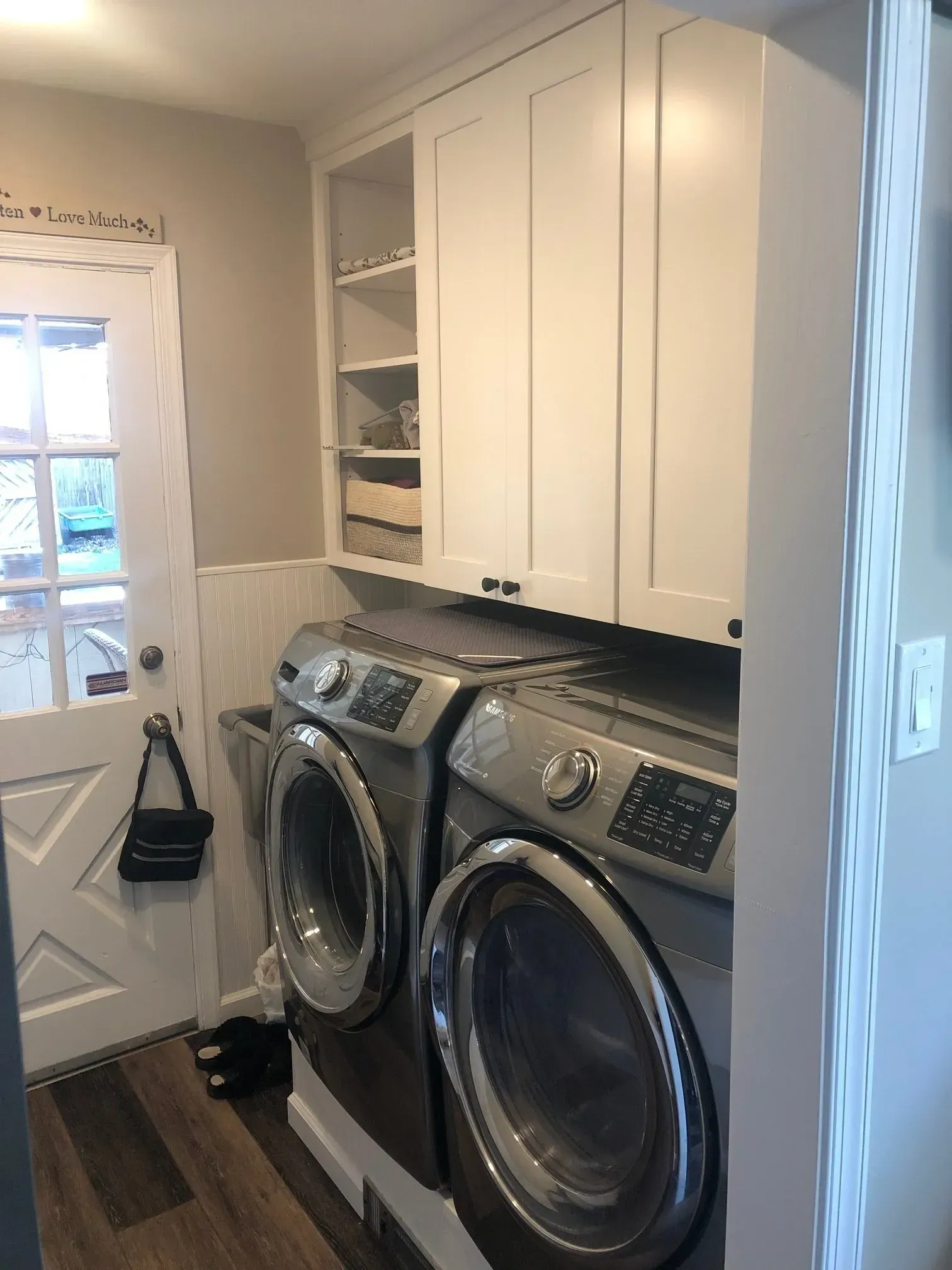 Laundry room with stacked washer and dryer, white cabinets, and a back door with daylight In Bucks County PA