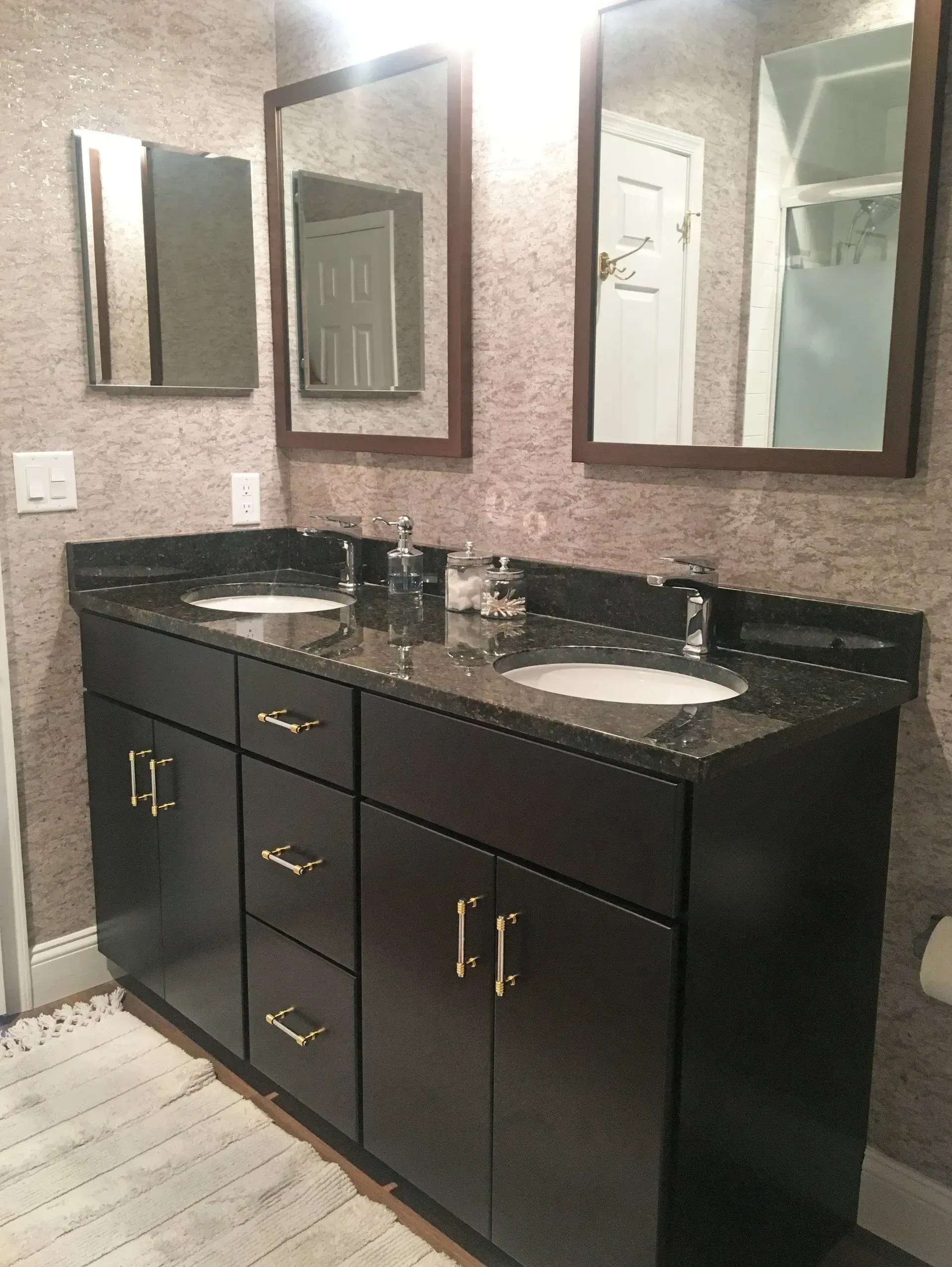 Modern double-sink bathroom vanity with black cabinets, granite countertop, and two mirrors against textured walls In Bucks County PA