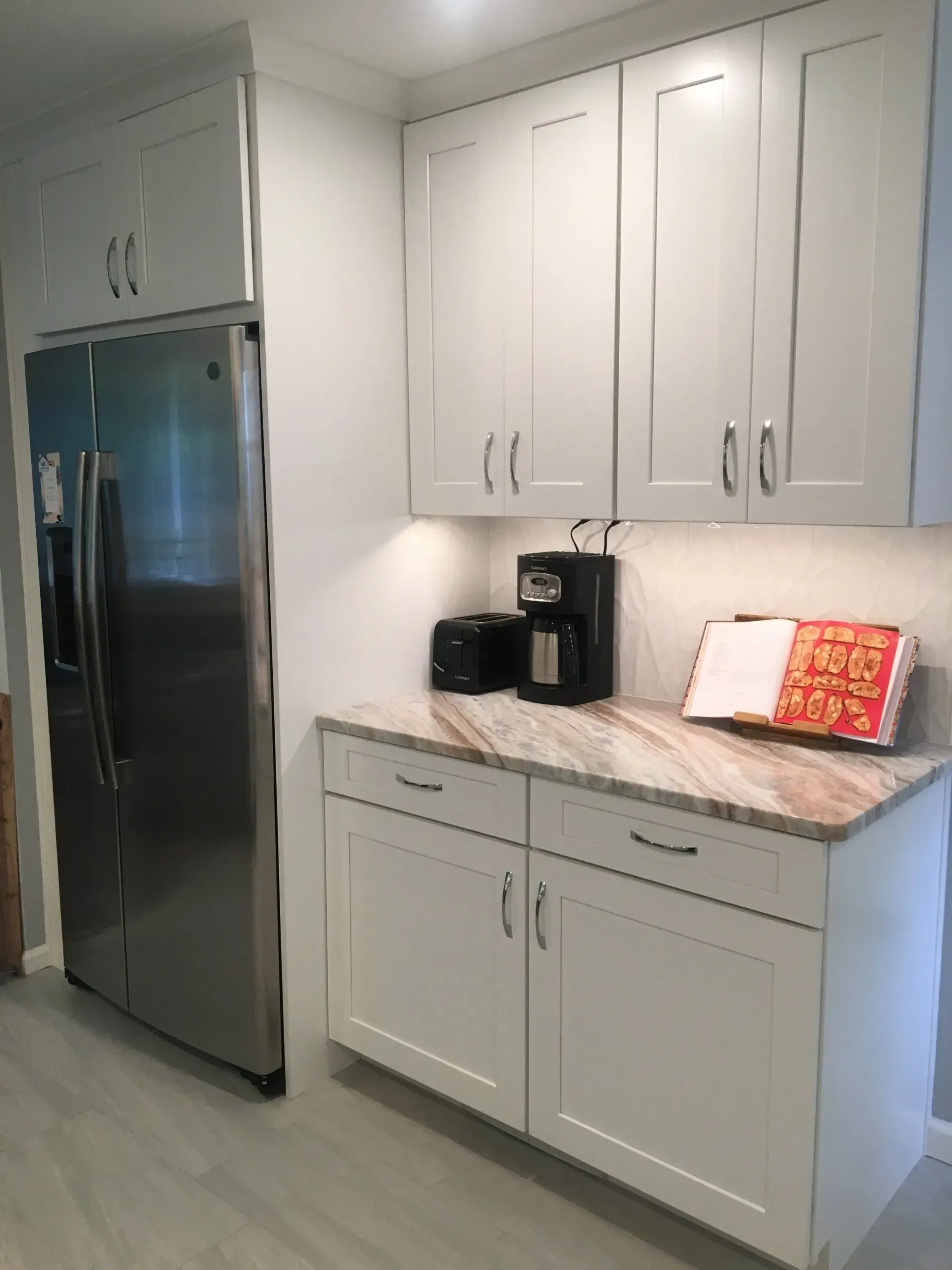 Kitchen with stainless steel refrigerator, white cabinets, marble countertop, and coffee maker In Bucks County PA
