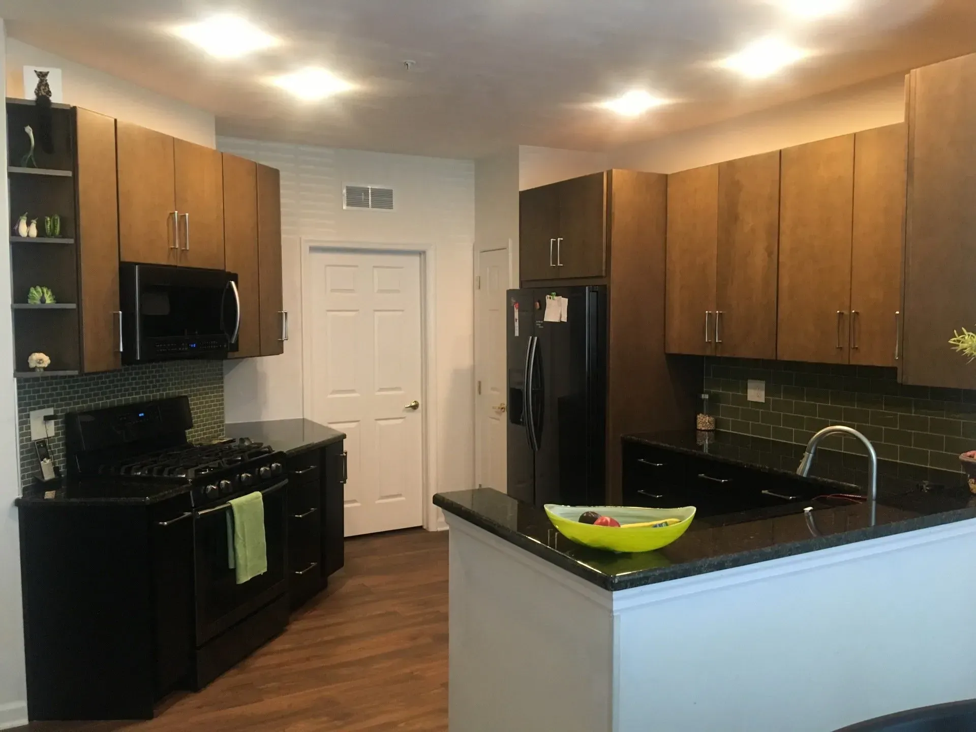 Modern kitchen with wood cabinets, black appliances, granite counters, and a white door at the back In Bucks Country PA