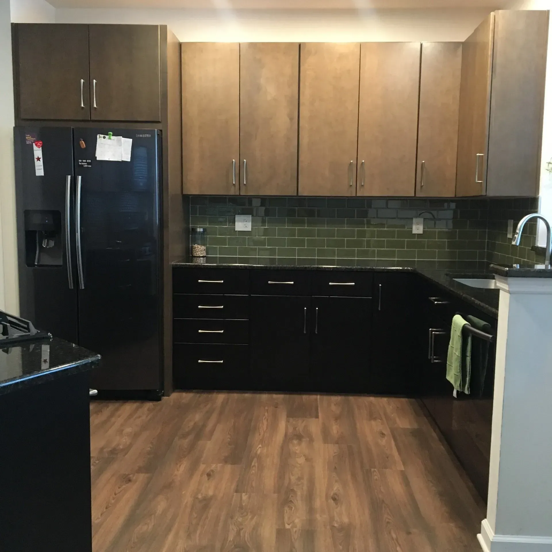 Modern kitchen with black appliances, wood cabinets, dark green backsplash, and wood flooring  In Bucks County PA
