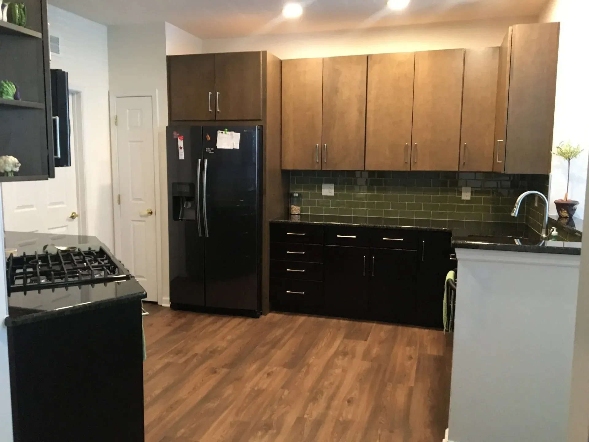 Modern kitchen with dark cabinets, black appliances, green tile backsplash, and wood flooring  In Bucks County PA