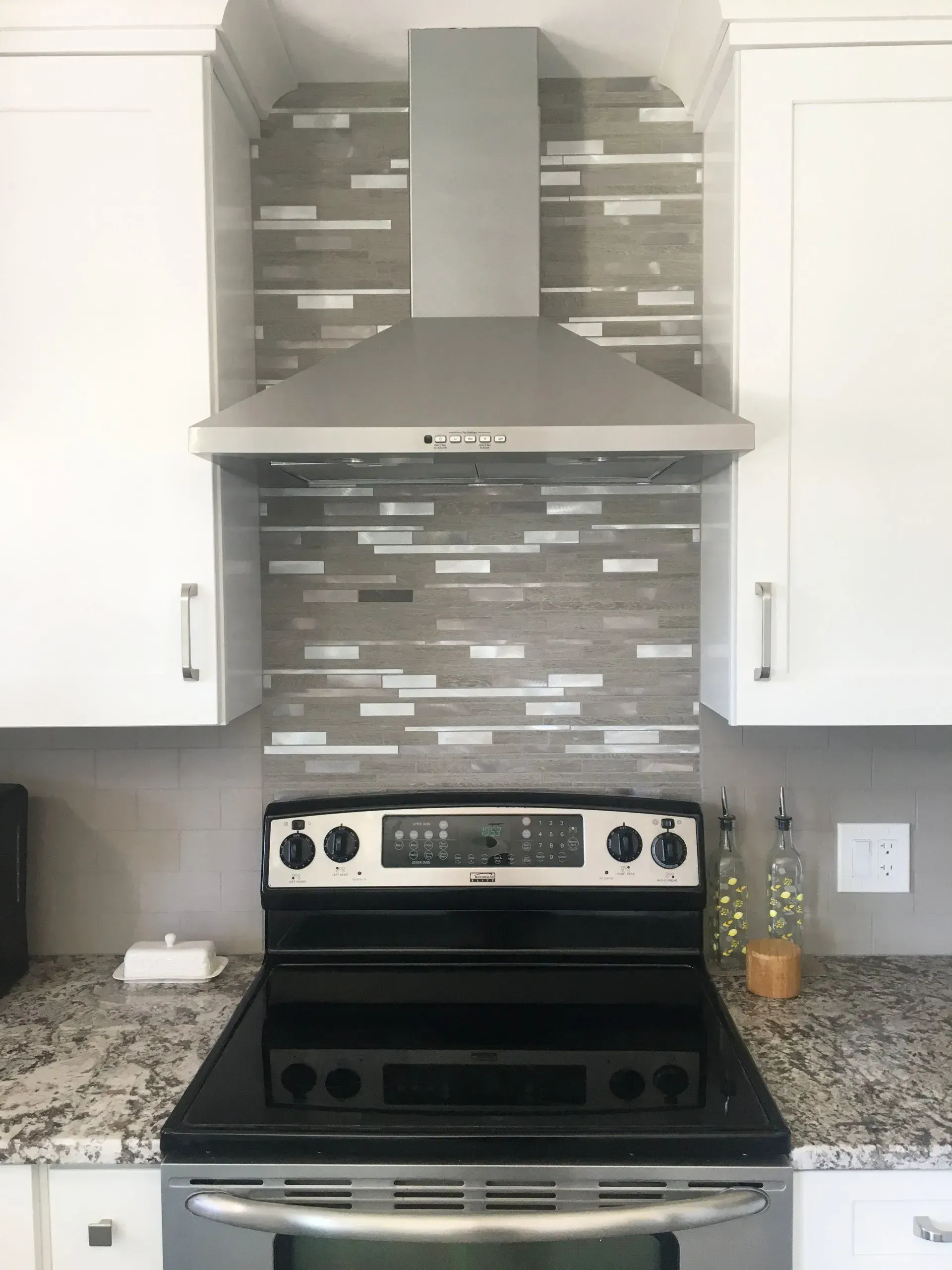 Modern kitchen with stainless steel stove and hood, gray tile backsplash, granite counters, and white cabinets In Bucks County PA
