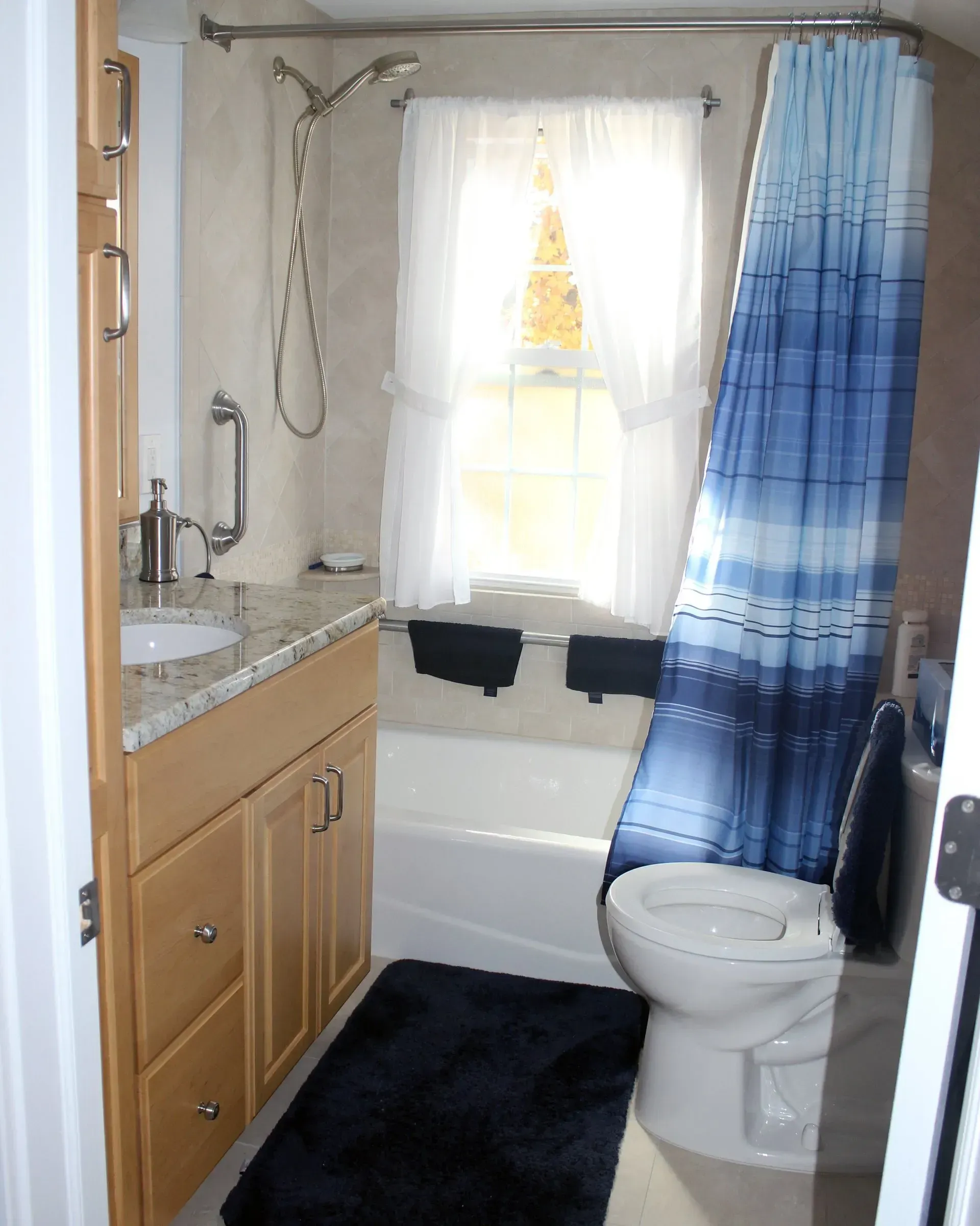Small bathroom with sink, toilet, blue shower curtain, and window above the tub In Bucks County PA