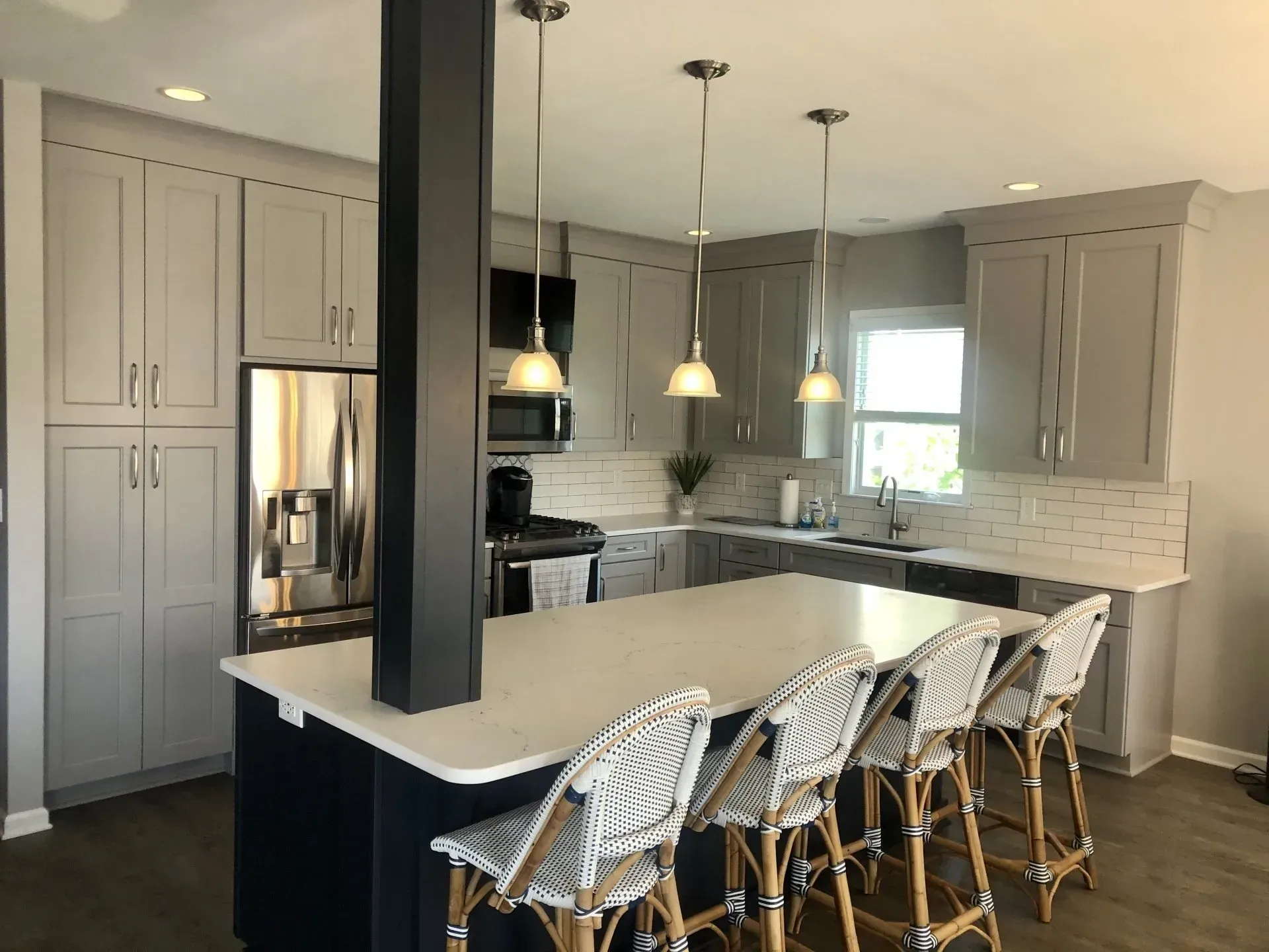 Modern kitchen with a white island, pendant lights, gray cabinets, and woven counter stools In Bucks County PA