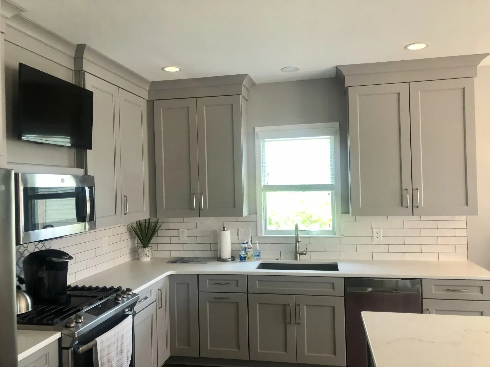 Modern kitchen with gray cabinets, white countertops, stainless appliances, and a window over the sink In Bucks County PA