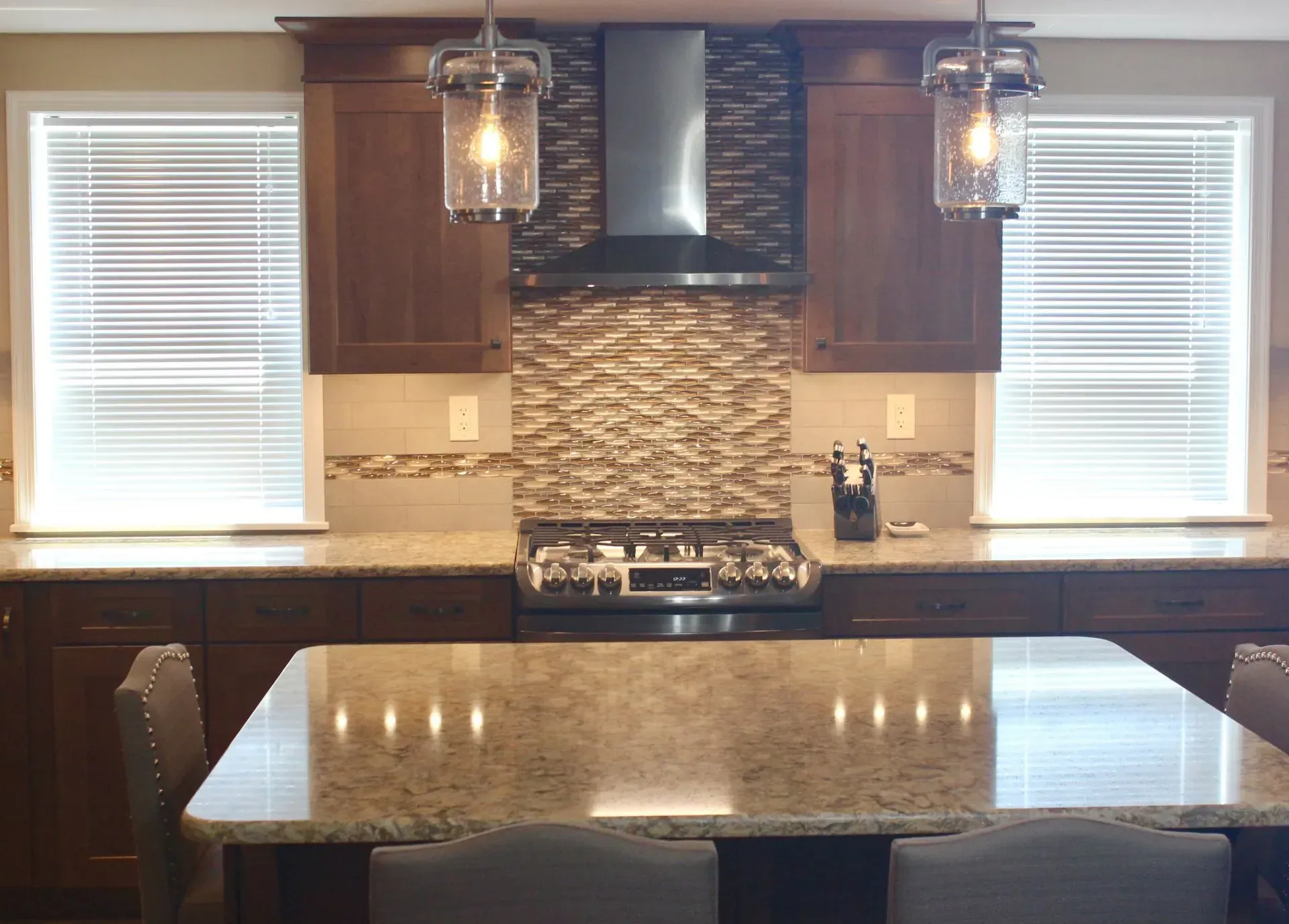 Modern kitchen with granite island, dark cabinets, pendant lights, and a stone backsplash  In Bucks County PA