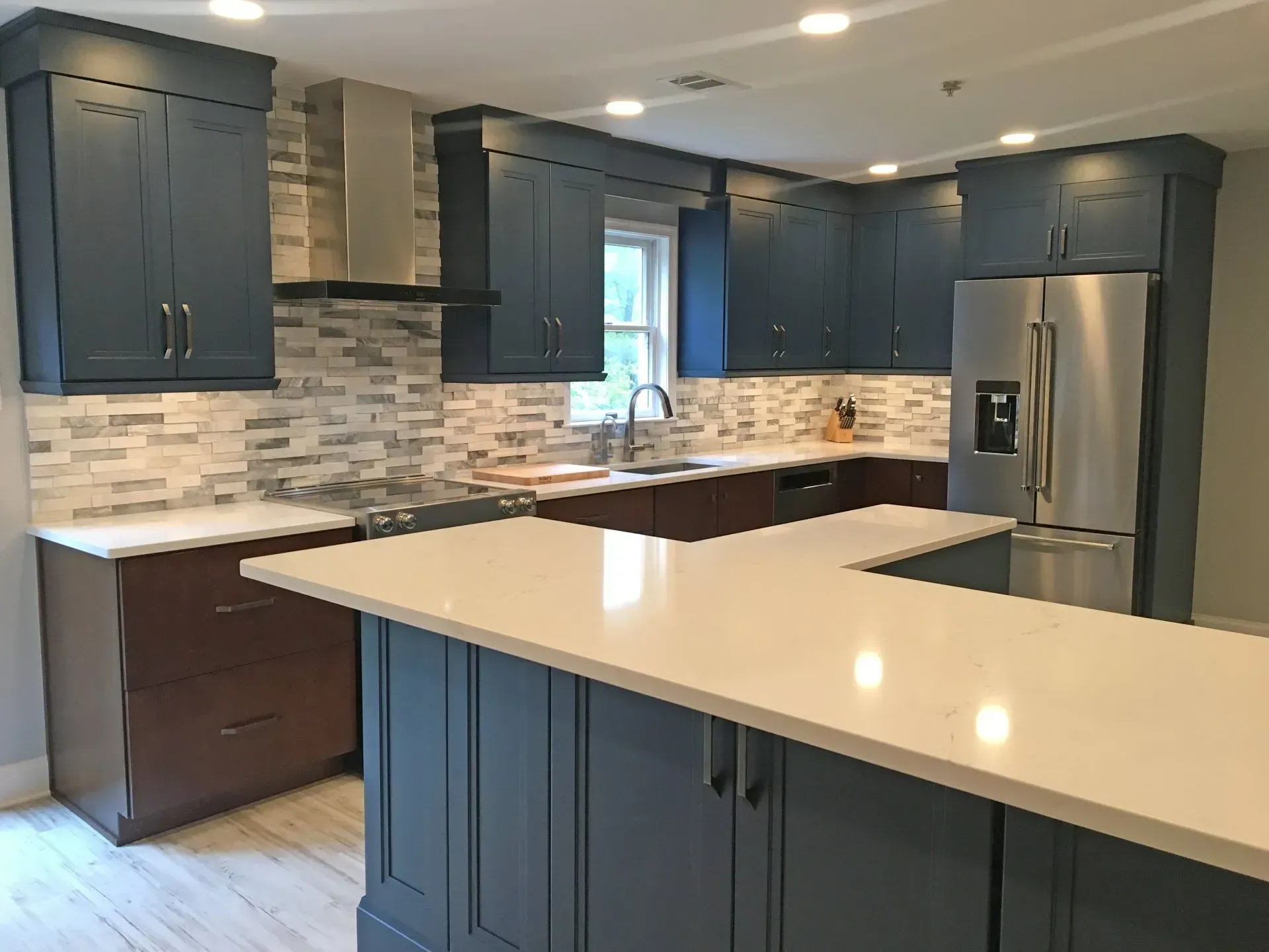 Modern kitchen with dark blue cabinets, white countertops, mosaic backsplash, and stainless steel refrigerator.In Bucks Country PA