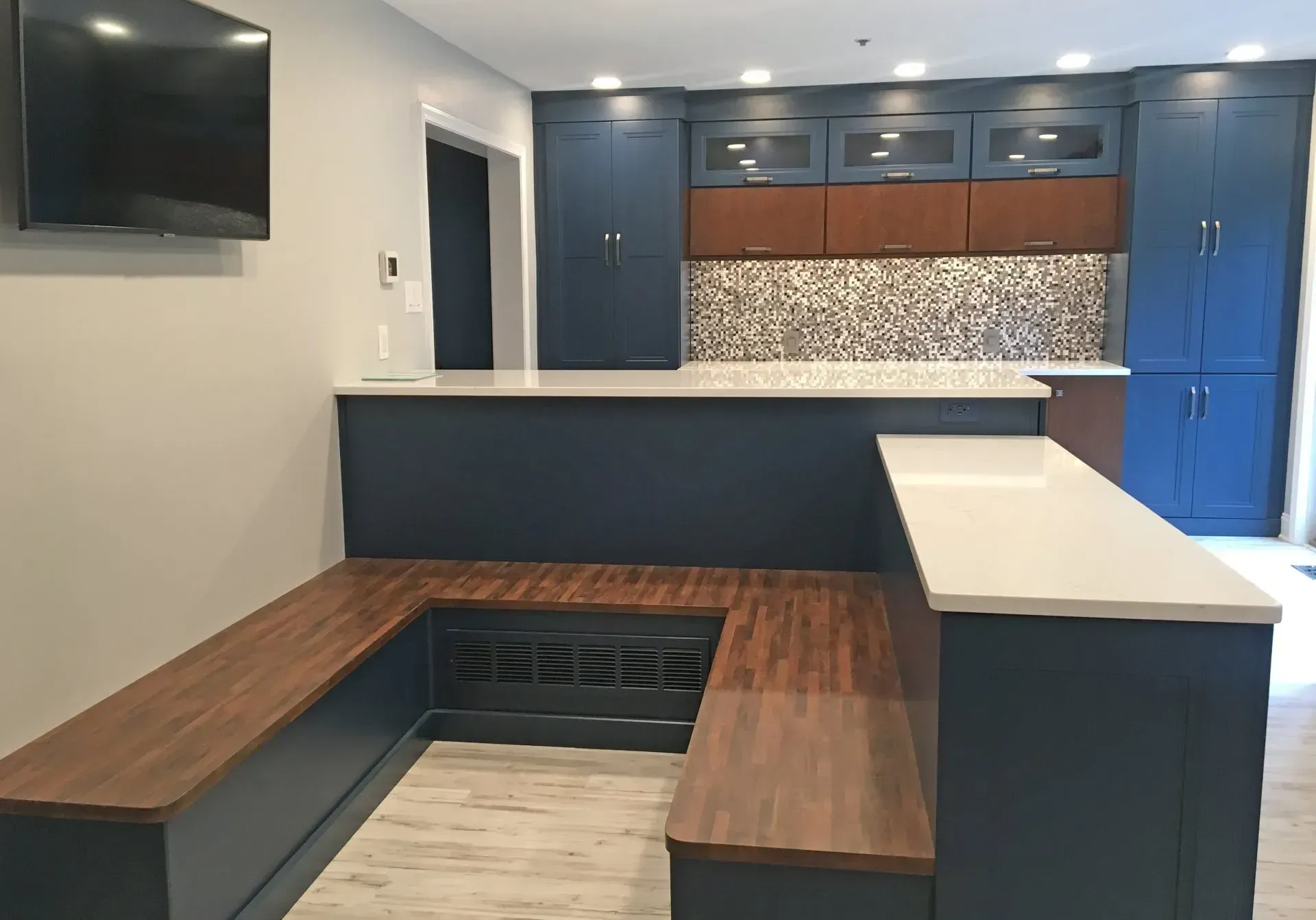 Modern kitchen with blue cabinets, wood benches, white island counter, and wall-mounted TV  In Bucks County PA