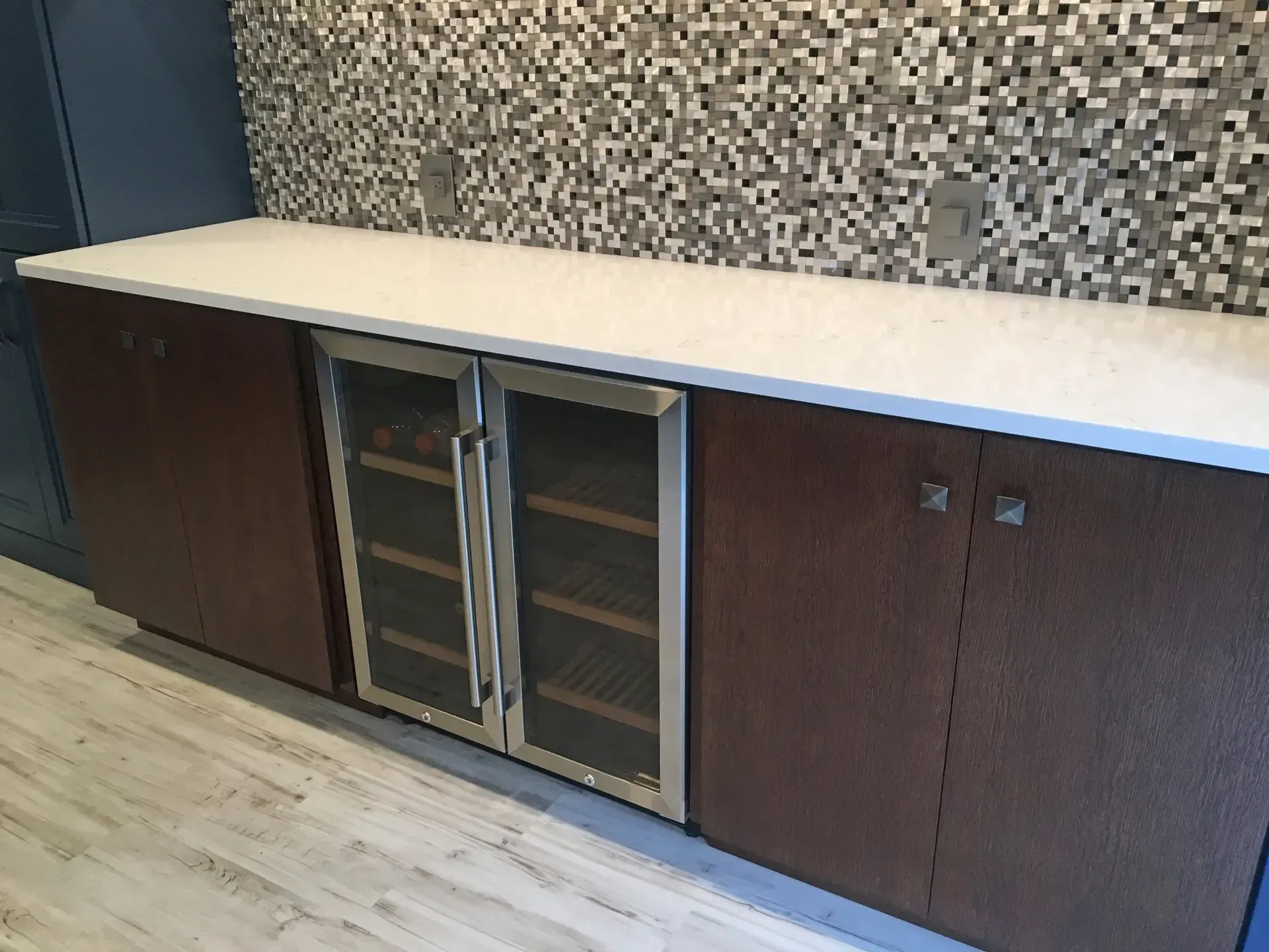 Built-in cabinet with glass-door mini fridge beneath a white countertop against a mosaic tile wall  In Bucks County PA