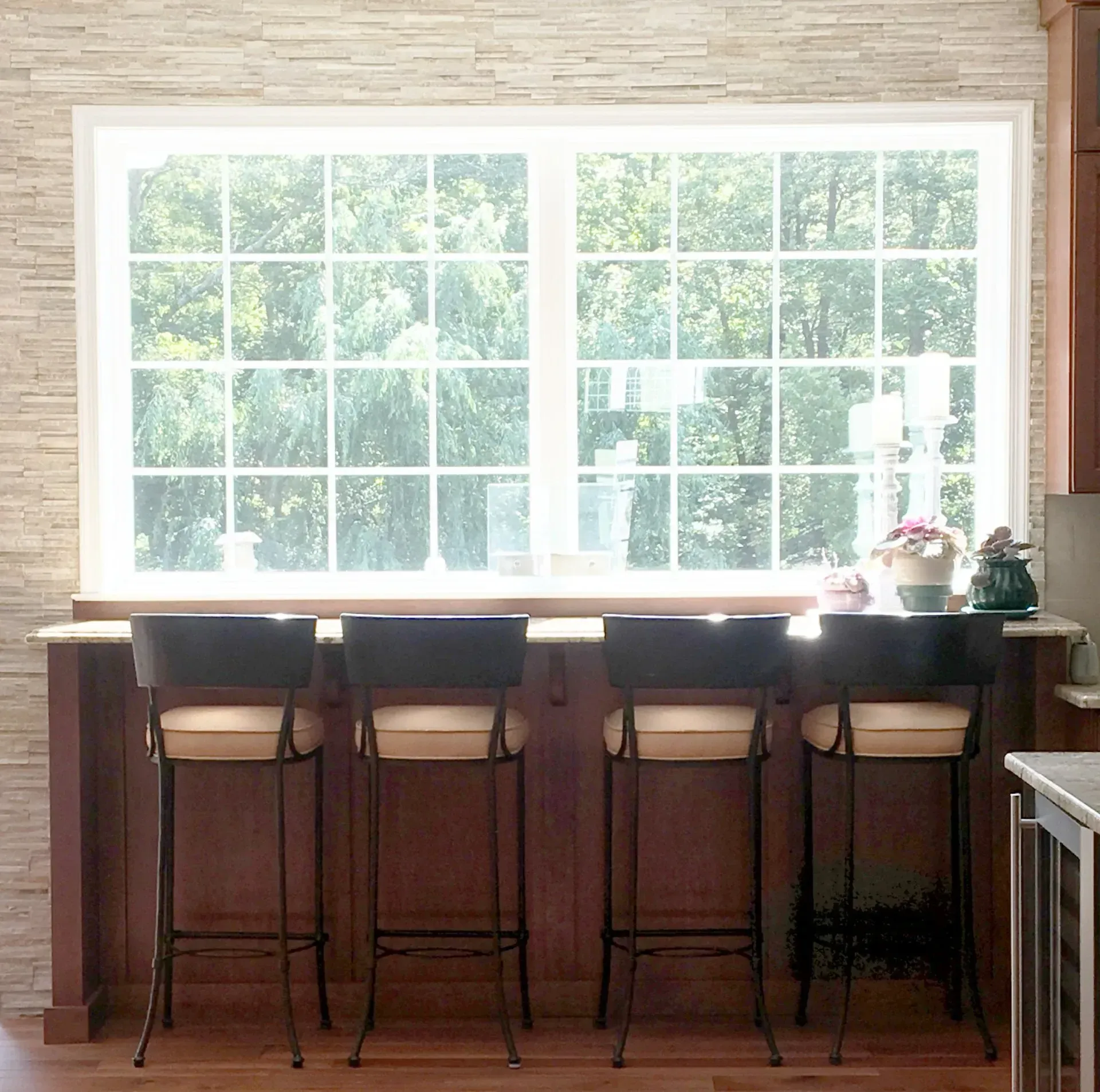 Bright kitchen window above a wooden breakfast bar with four tall stools and potted plants on the right In Bucks Country PA
