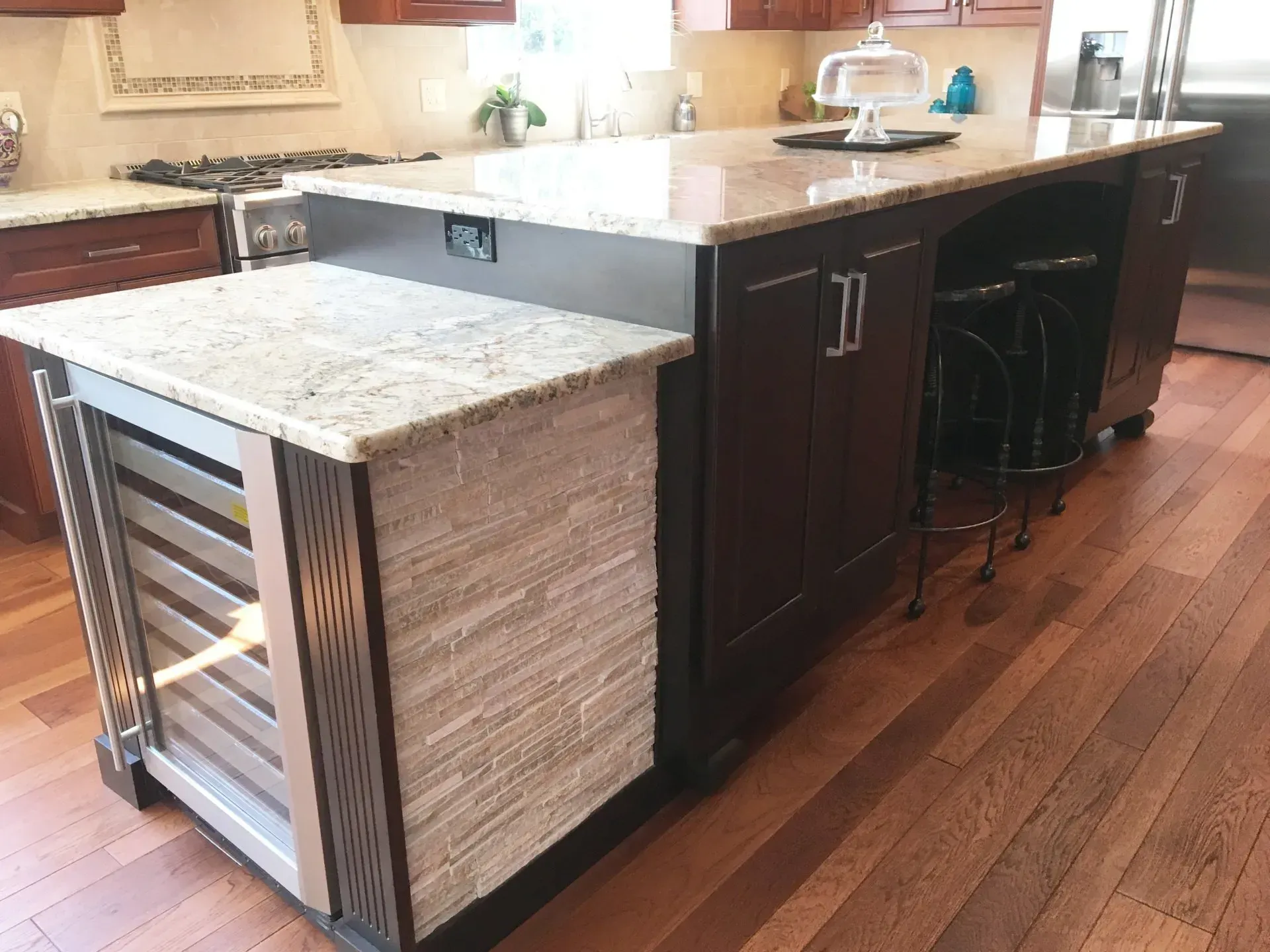 Kitchen island with granite countertop, built-in wine rack, and dark wood cabinets on hardwood floor In Bucks Country PA