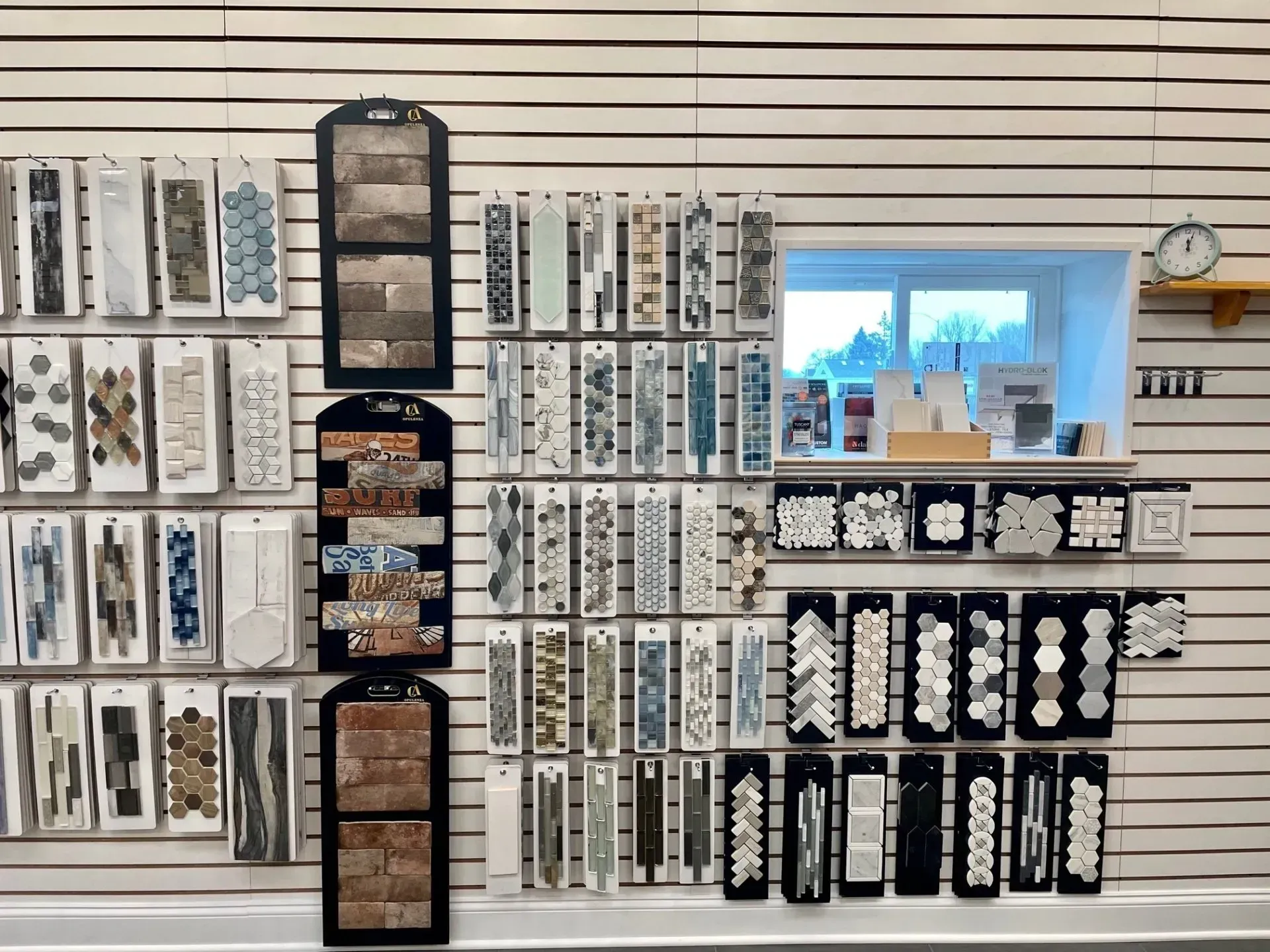 Wall display of packaged samples and product cards on slatwall shelves, with a small window and clock on the right  In Bucks County PA